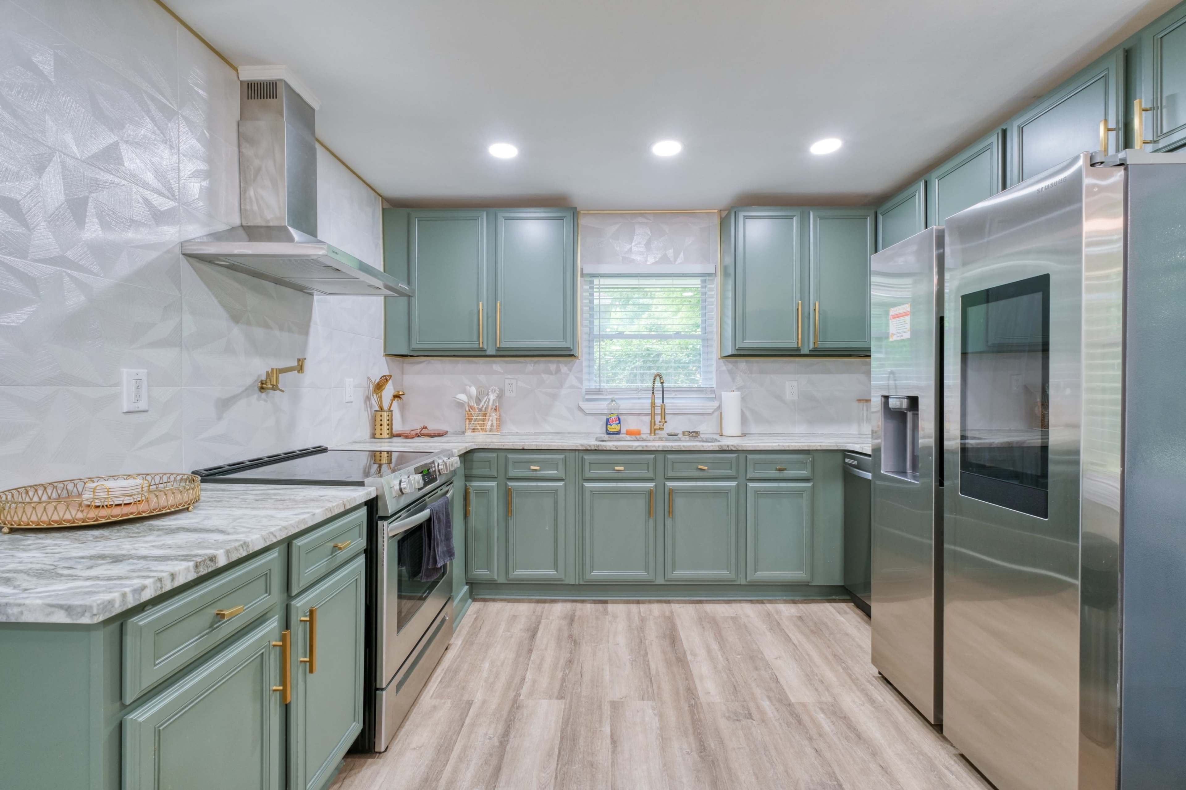 A modern kitchen features green cabinets, marble countertops, and stainless steel appliances.