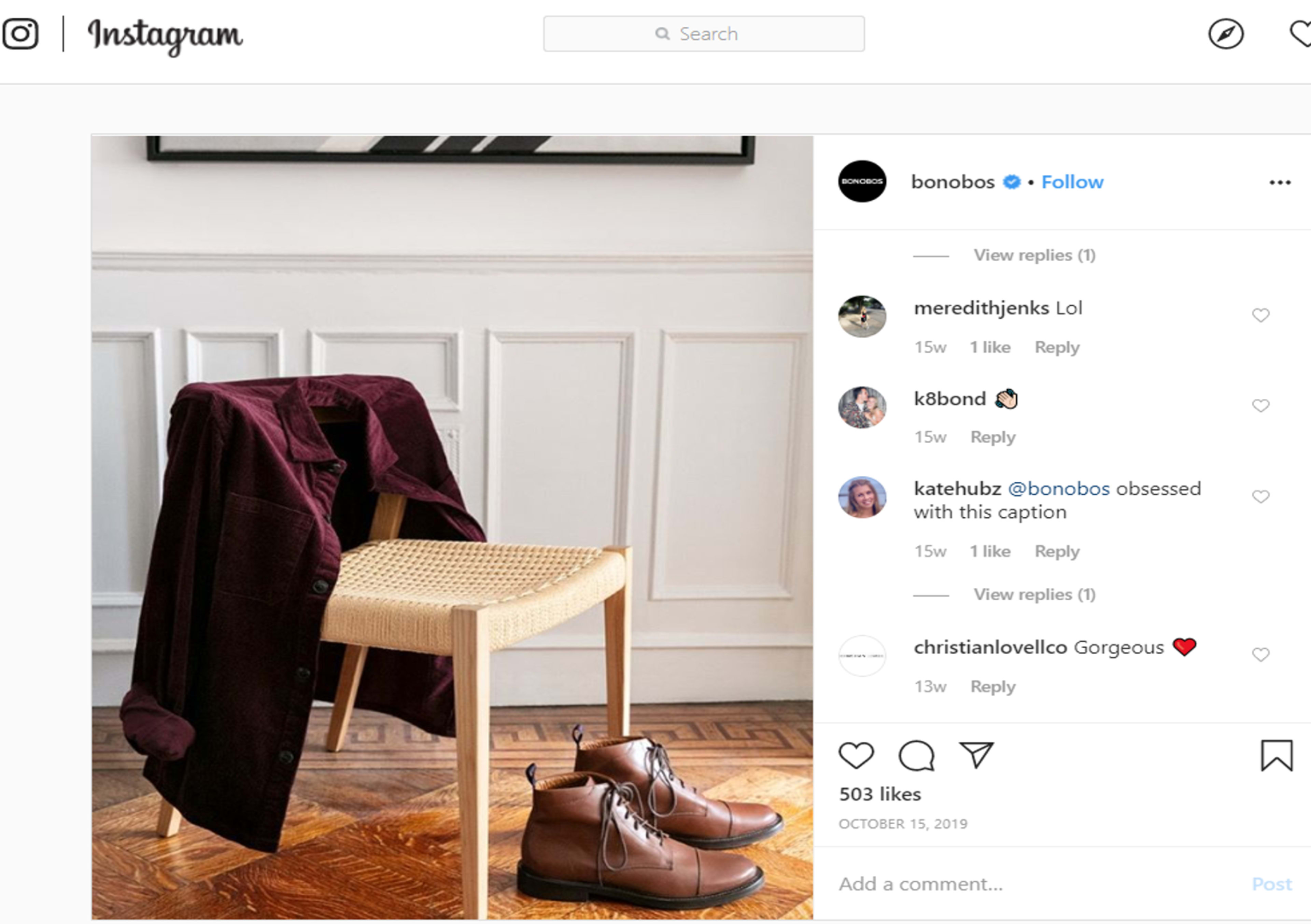 A maroon shirt is draped over a wooden chair beside a pair of brown boots on a patterned floor.