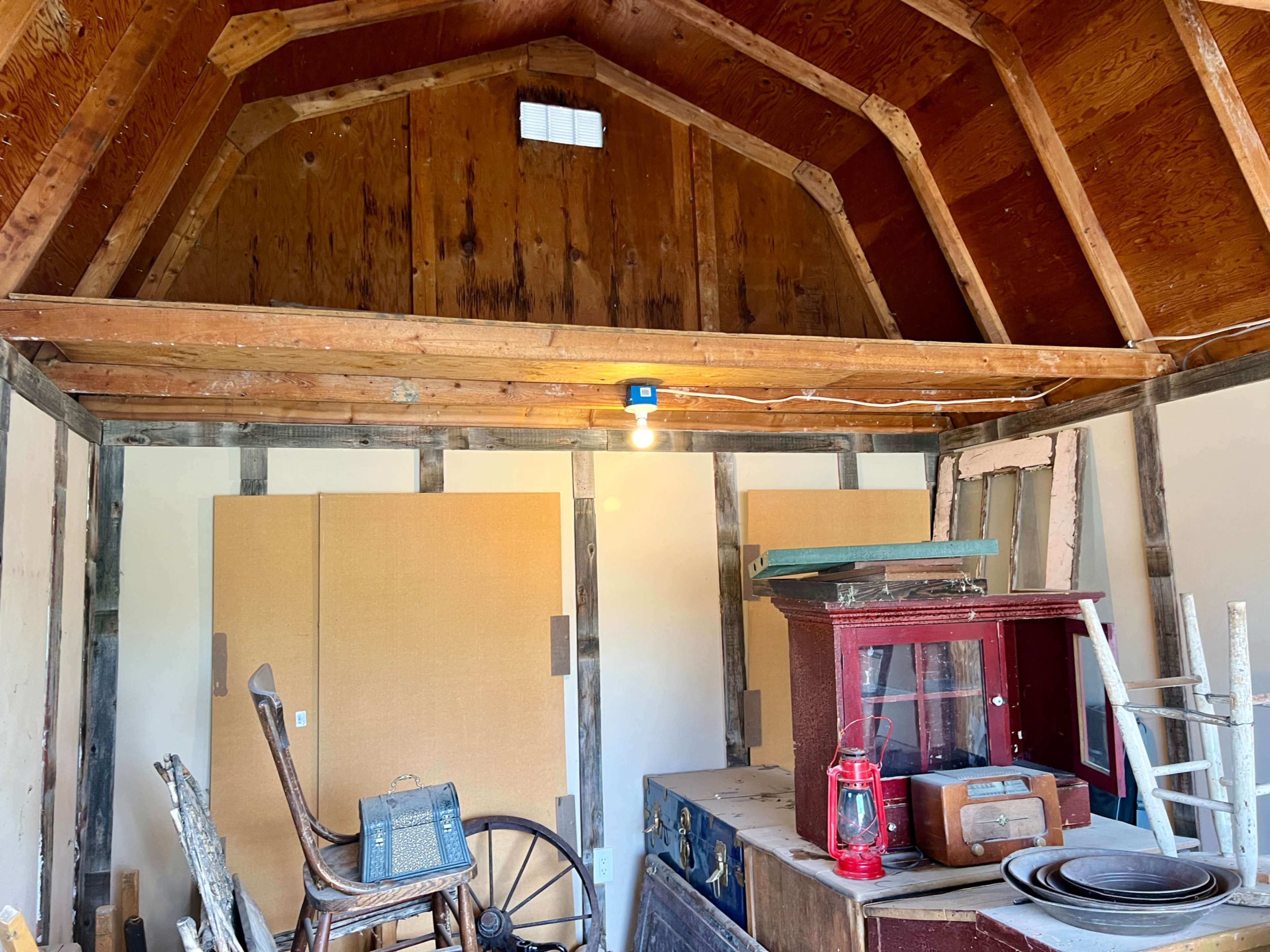 The image shows the interior of a rustic wooden building with exposed beams, featuring various vintage items, including a lantern and a wooden cart wheel.