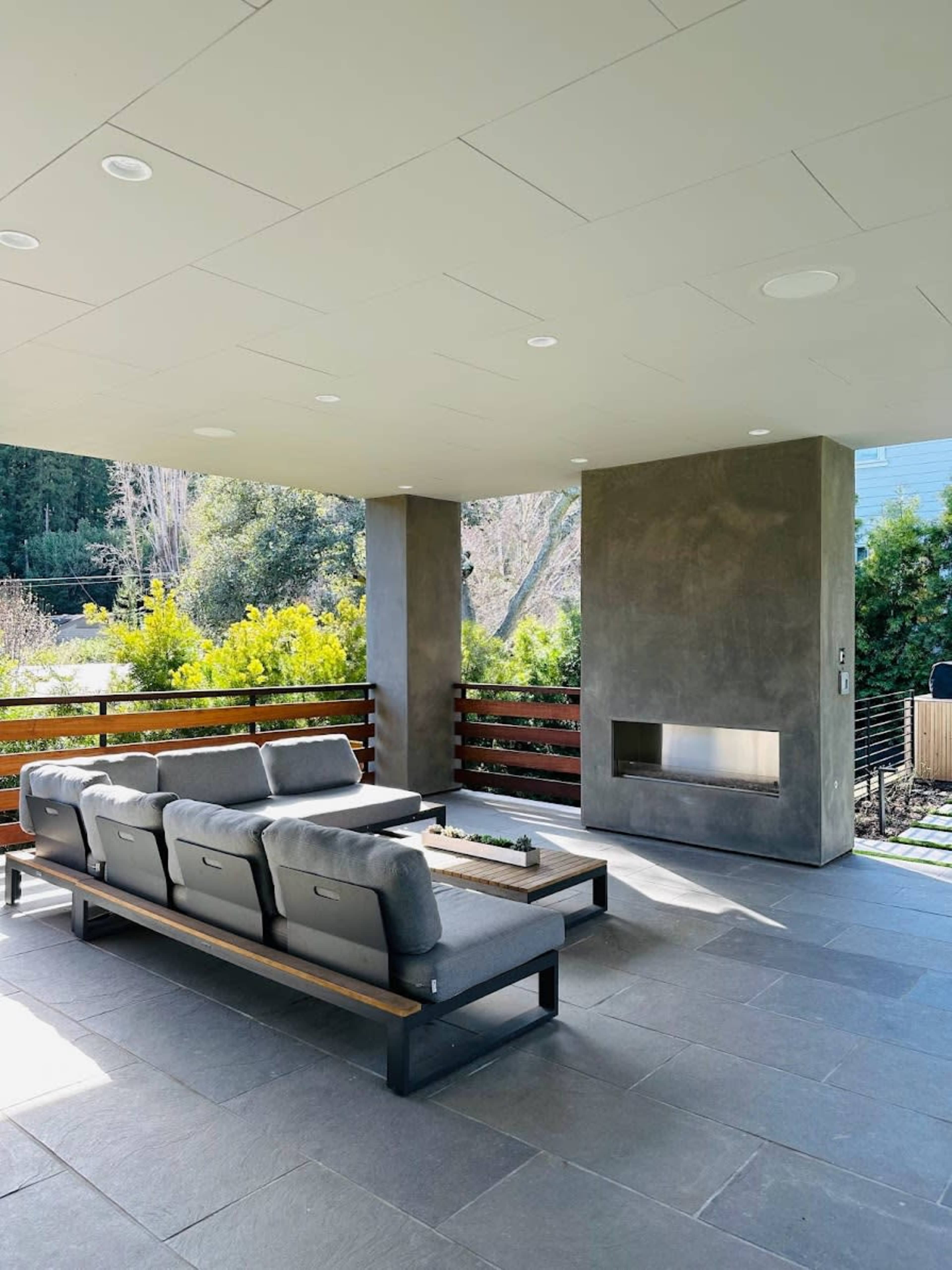 A modern covered patio area featuring a sectional sofa and a built-in fireplace.