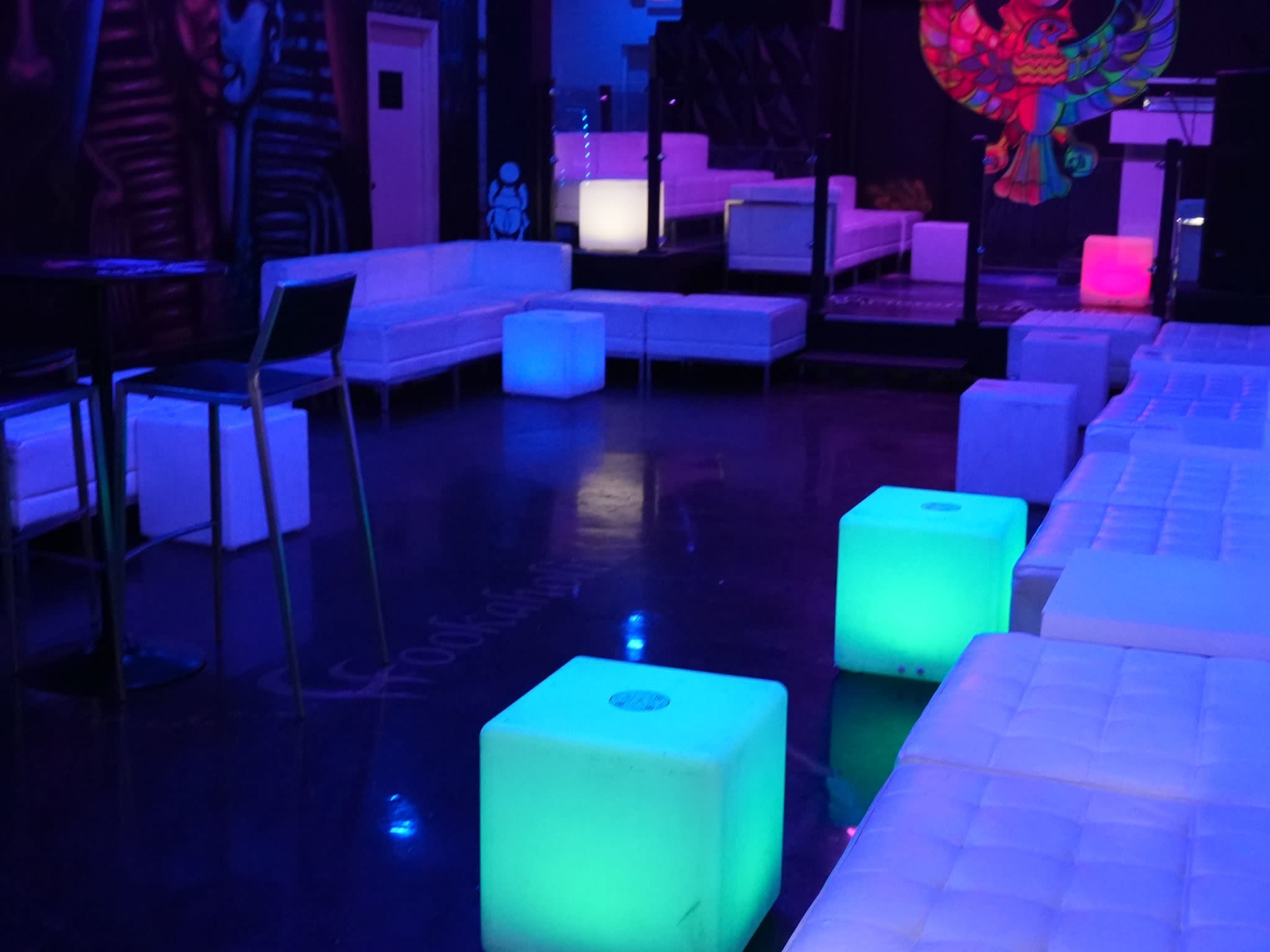 A dimly lit lounge area with white couches and illuminated cubes in shades of blue and green.