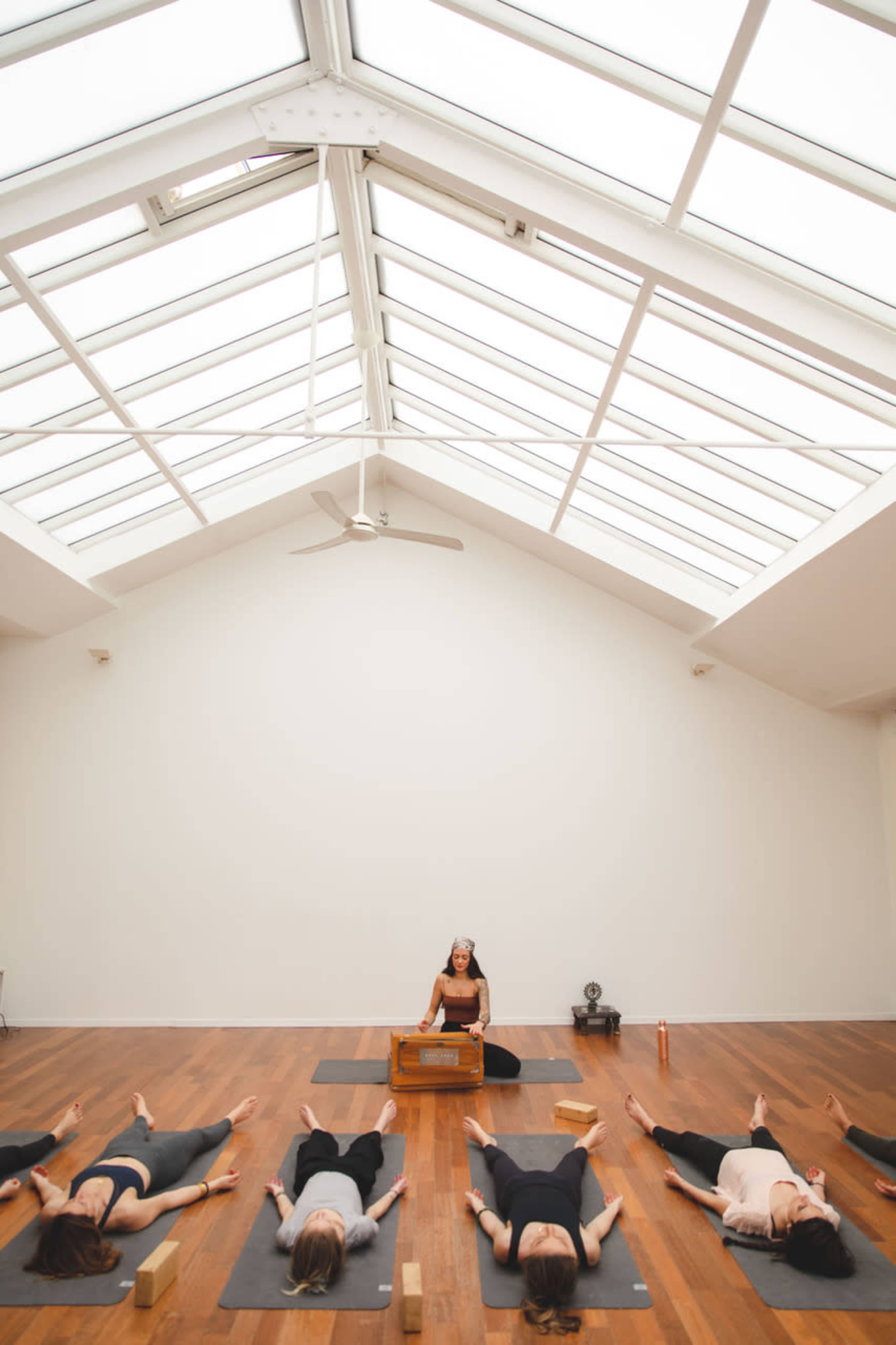 A group of people are practicing yoga in a bright, spacious studio, with a teacher positioned at the front.