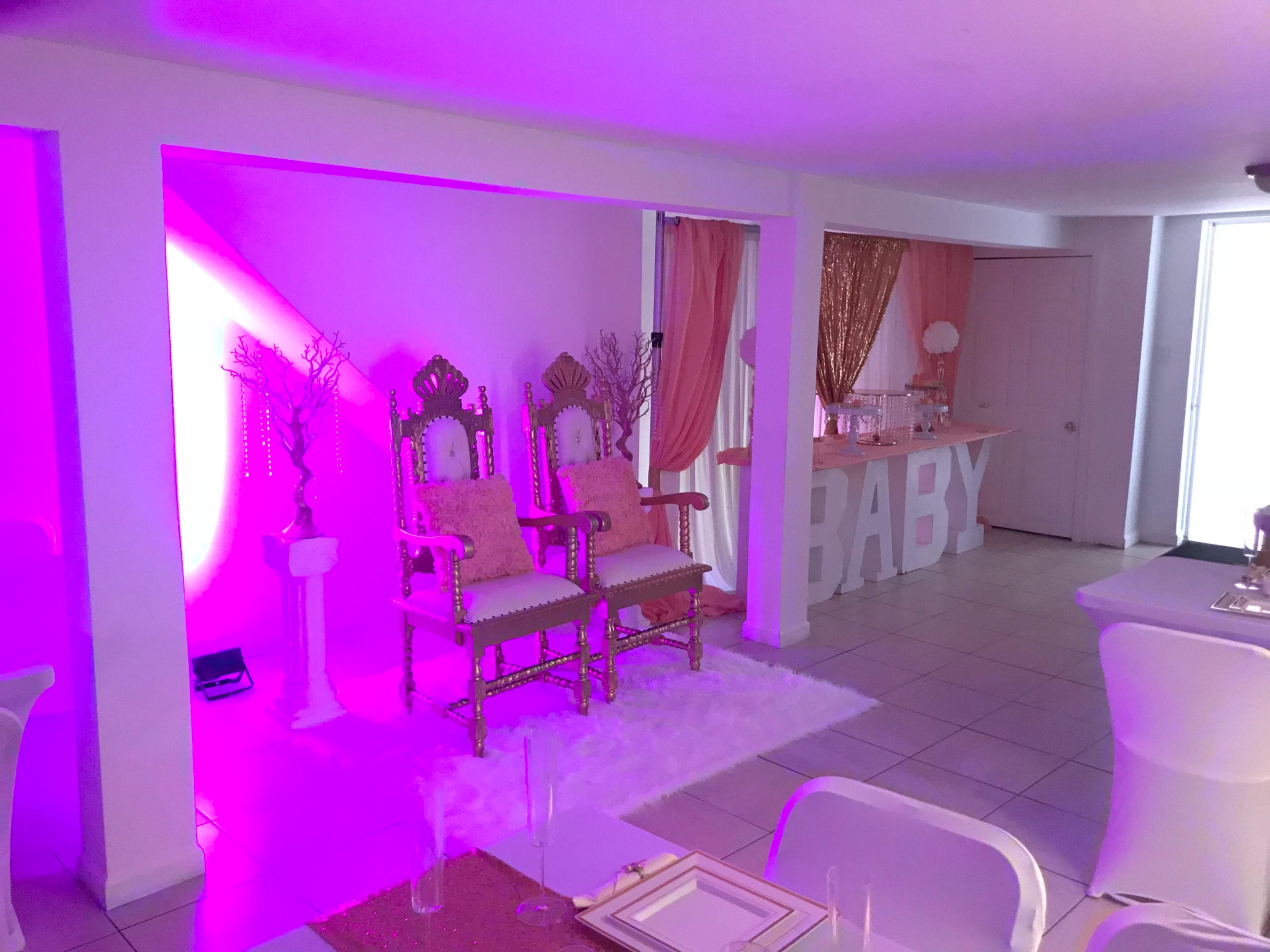 A decorated party space with two ornate chairs, a pink-themed backdrop, and a large "BABY" sign.