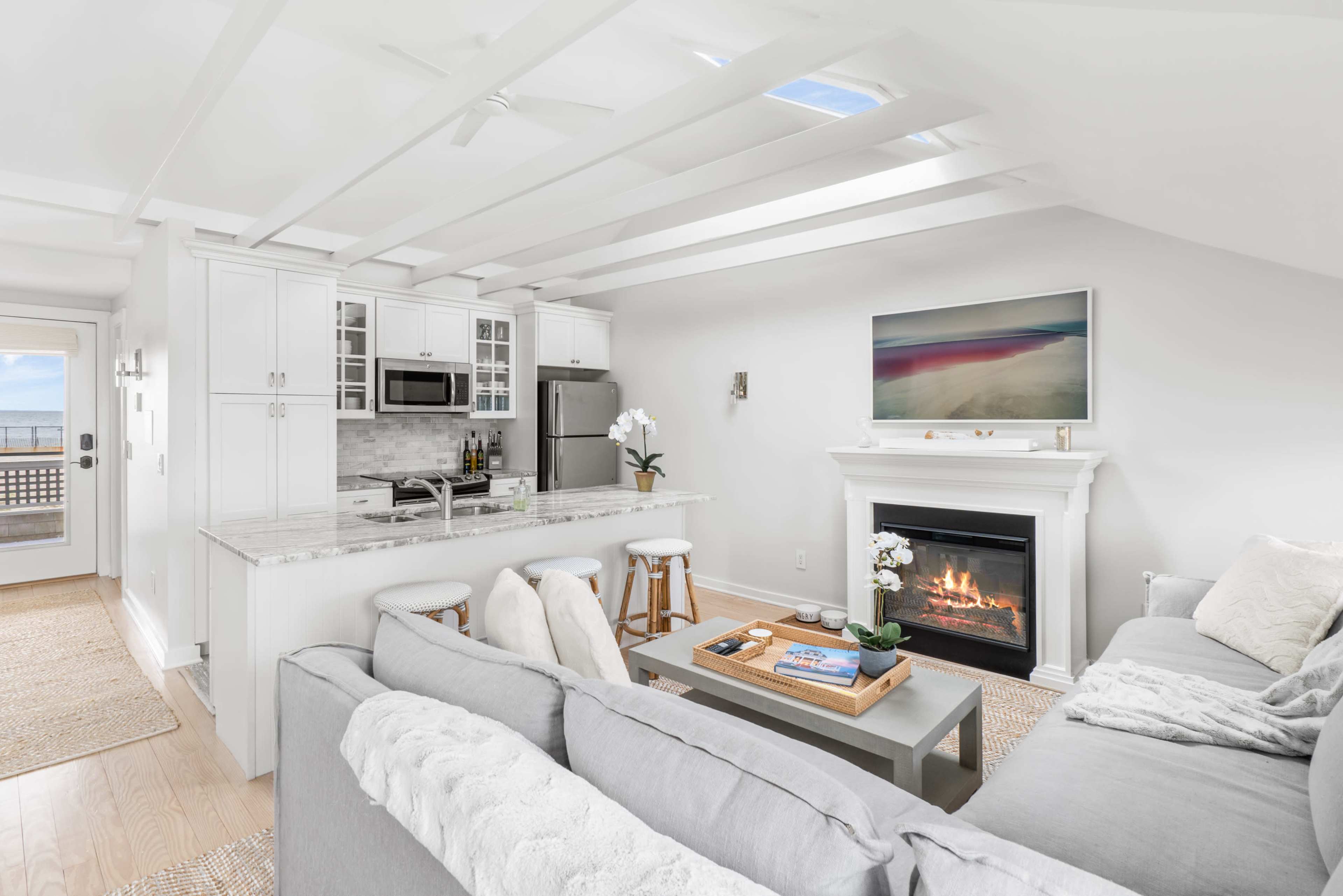 A modern living area features a kitchen, a seating area with a sofa, and a fireplace, all illuminated by natural light from the skylight.