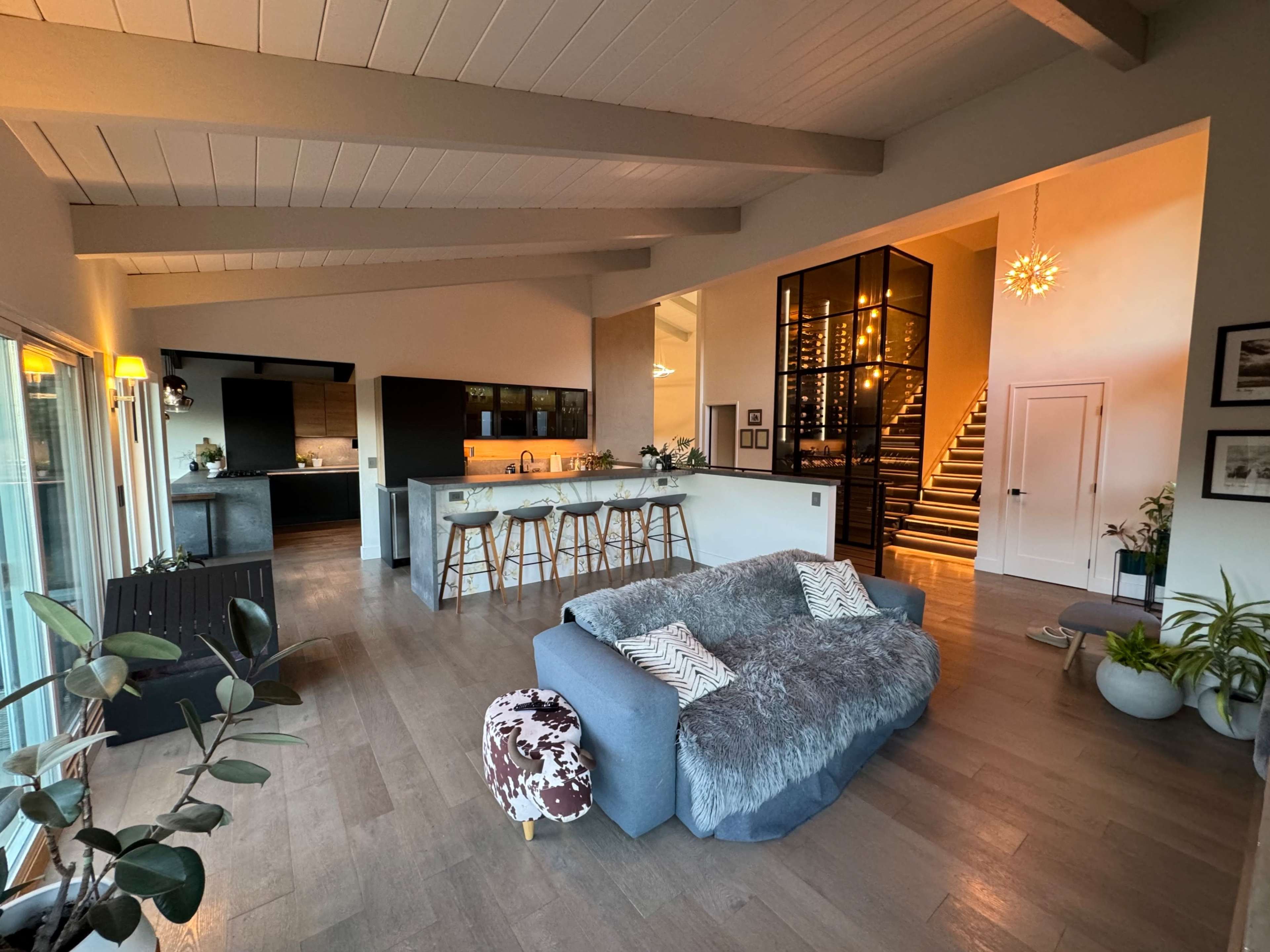 A modern, open-concept living space with a cozy gray sofa, a kitchen with bar seating, and a staircase leading to an upper level.