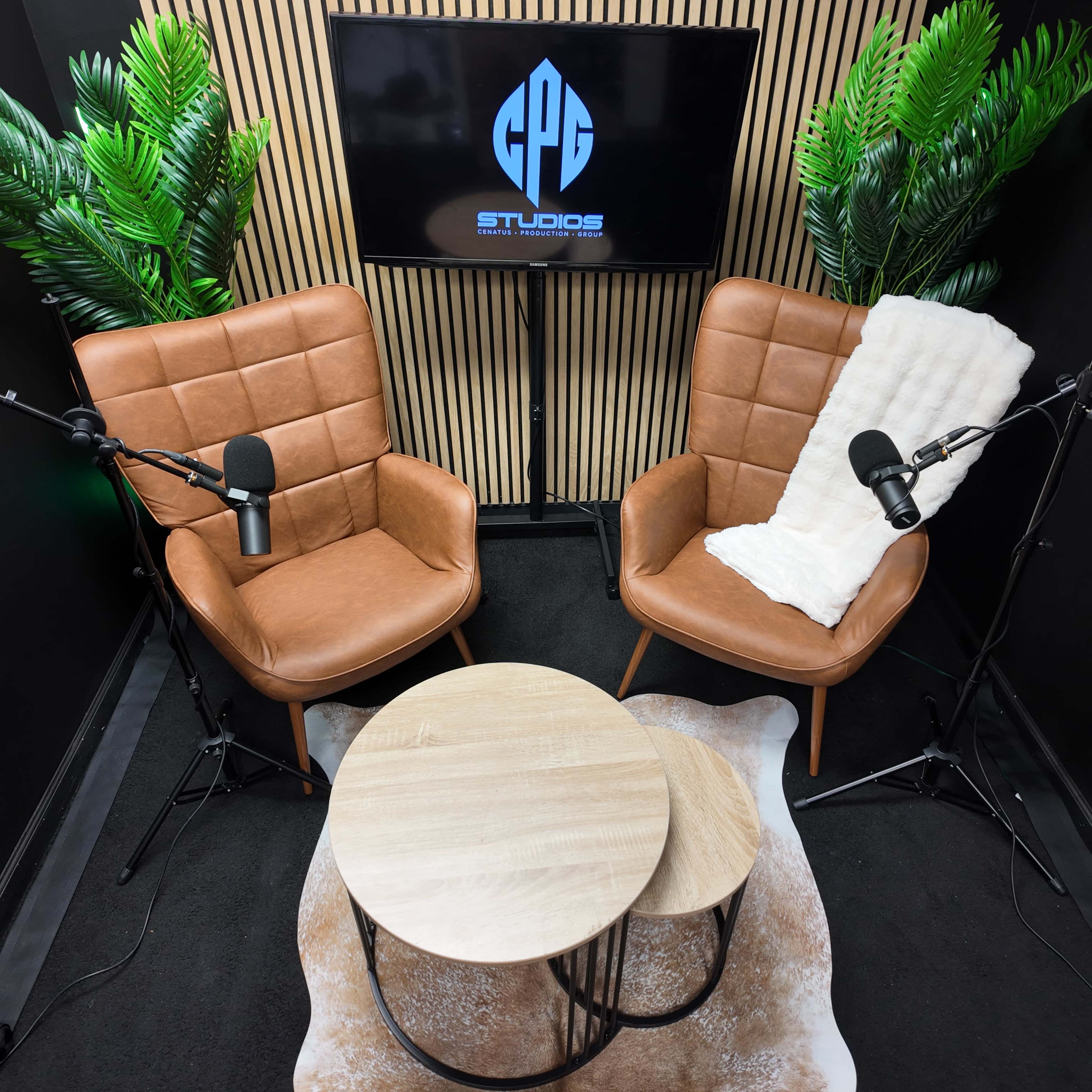 The image shows a podcast recording set with two leather chairs, a small round wooden table, and a screen displaying the logo "GPG Studios," surrounded by artificial plants.
