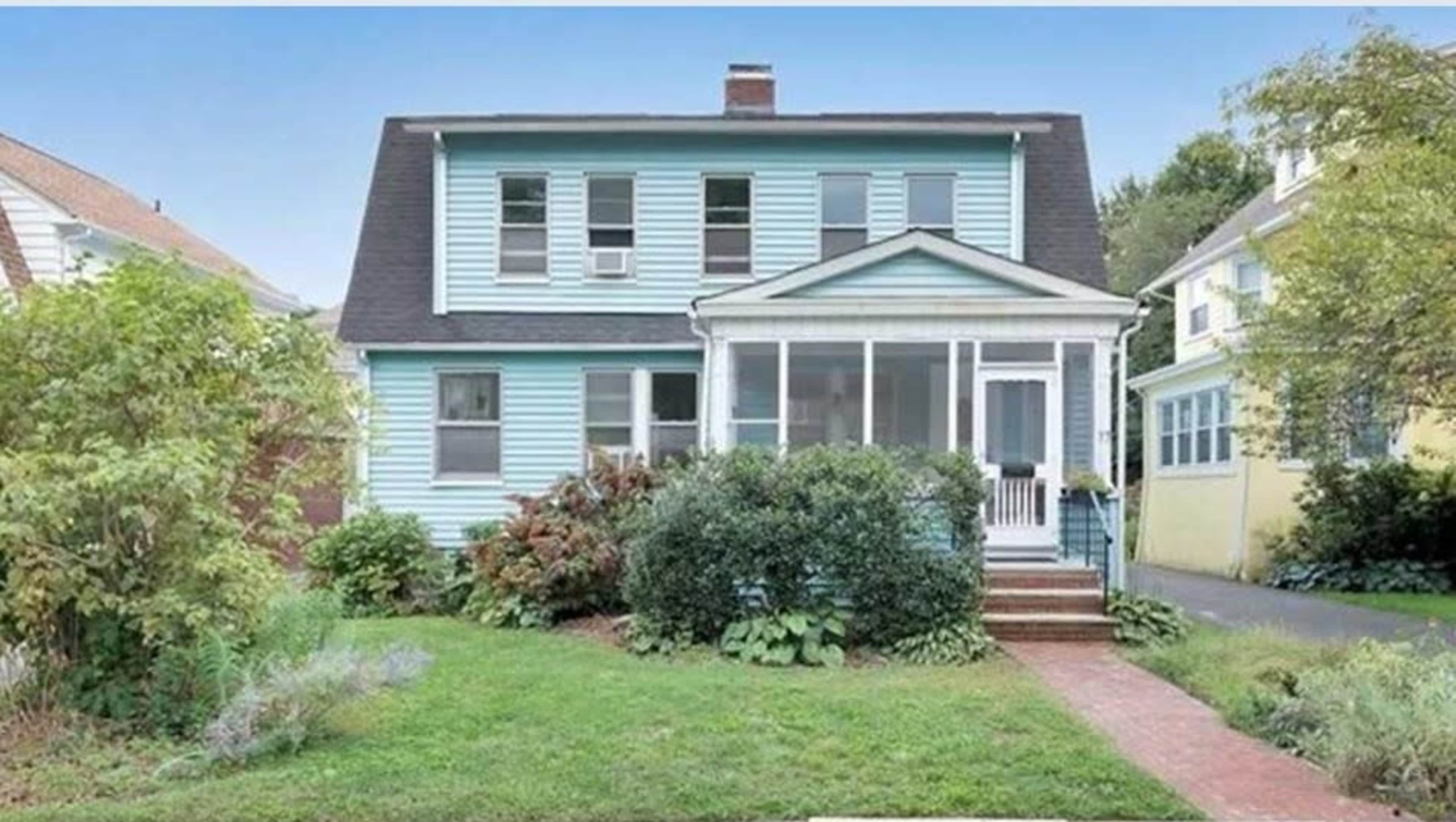 A two-story blue house with a front porch and surrounding greenery.