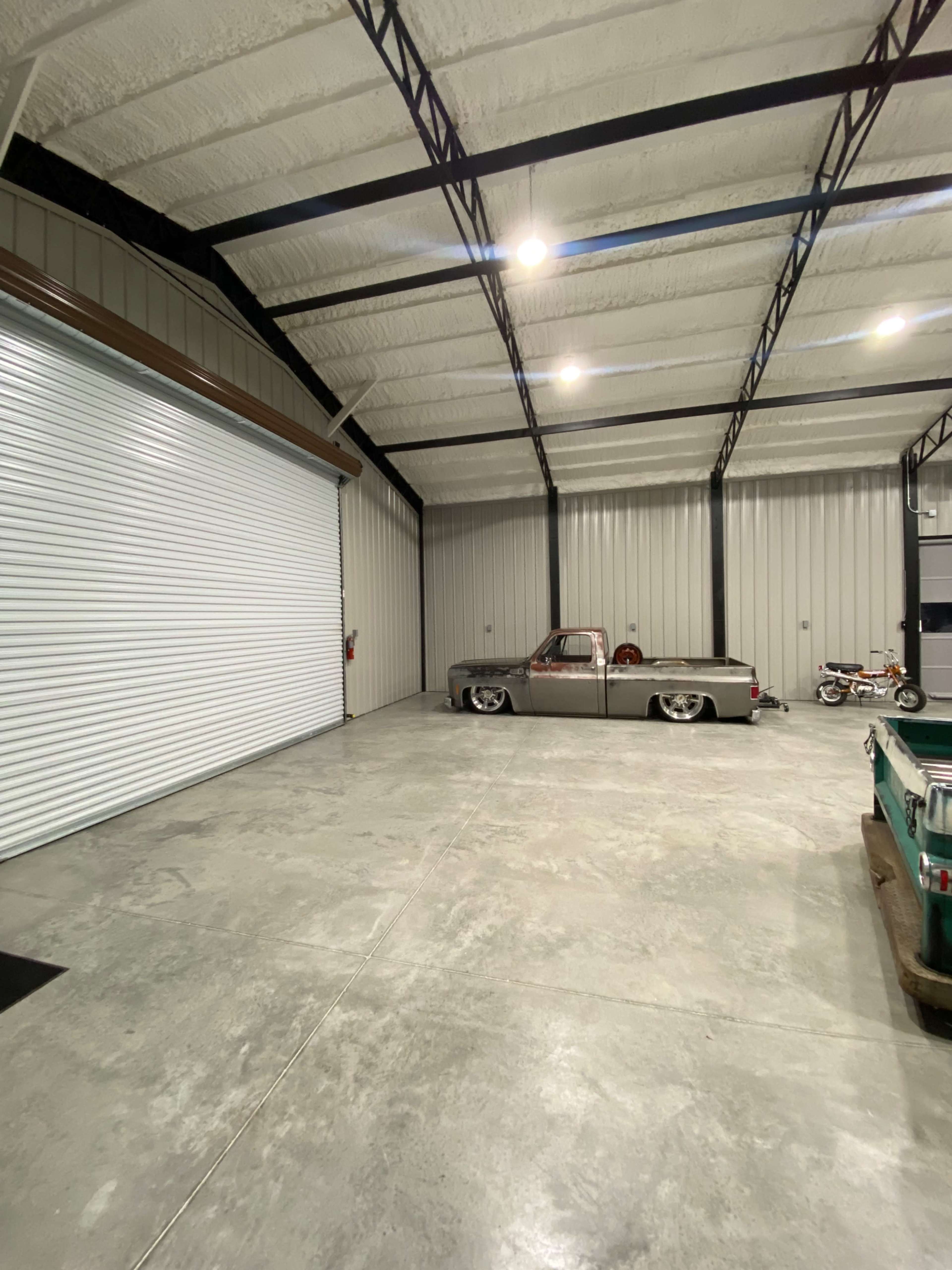 The image shows a spacious garage with a silver pickup truck parked on a polished concrete floor, alongside a motorcycle and a large roll-up door.