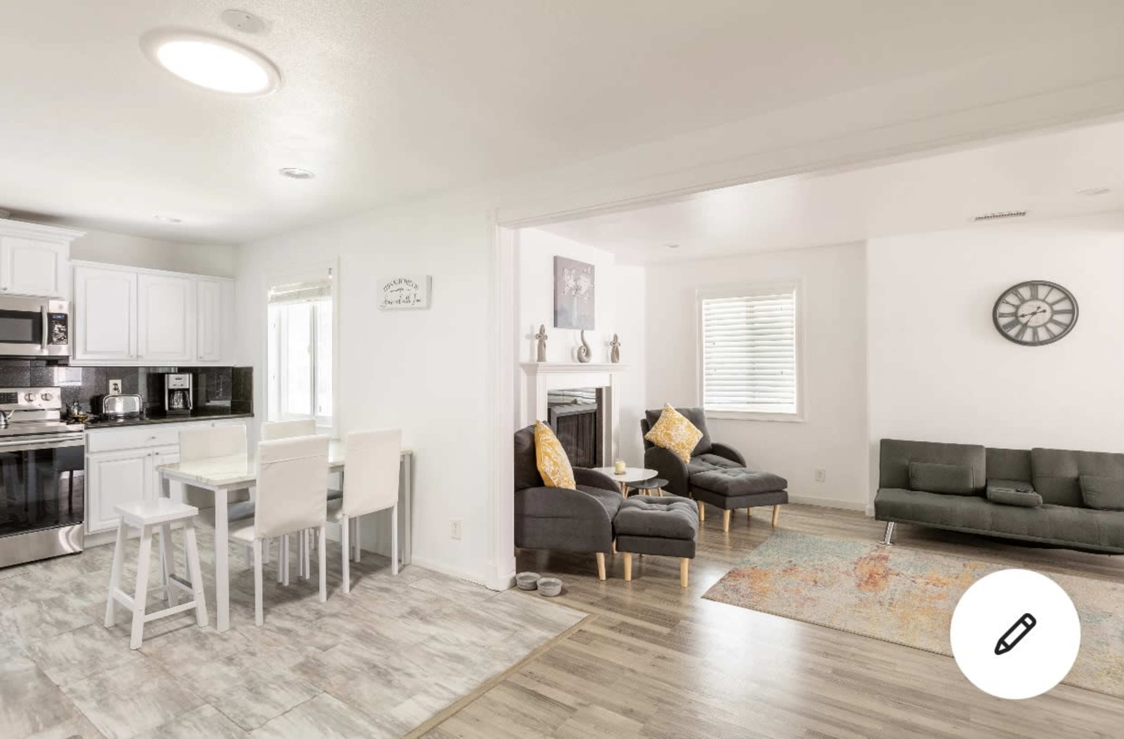 A modern open-concept living space features a kitchen with white cabinets and stainless steel appliances, adjacent to a cozy seating area with a gray sofa and two armchairs.