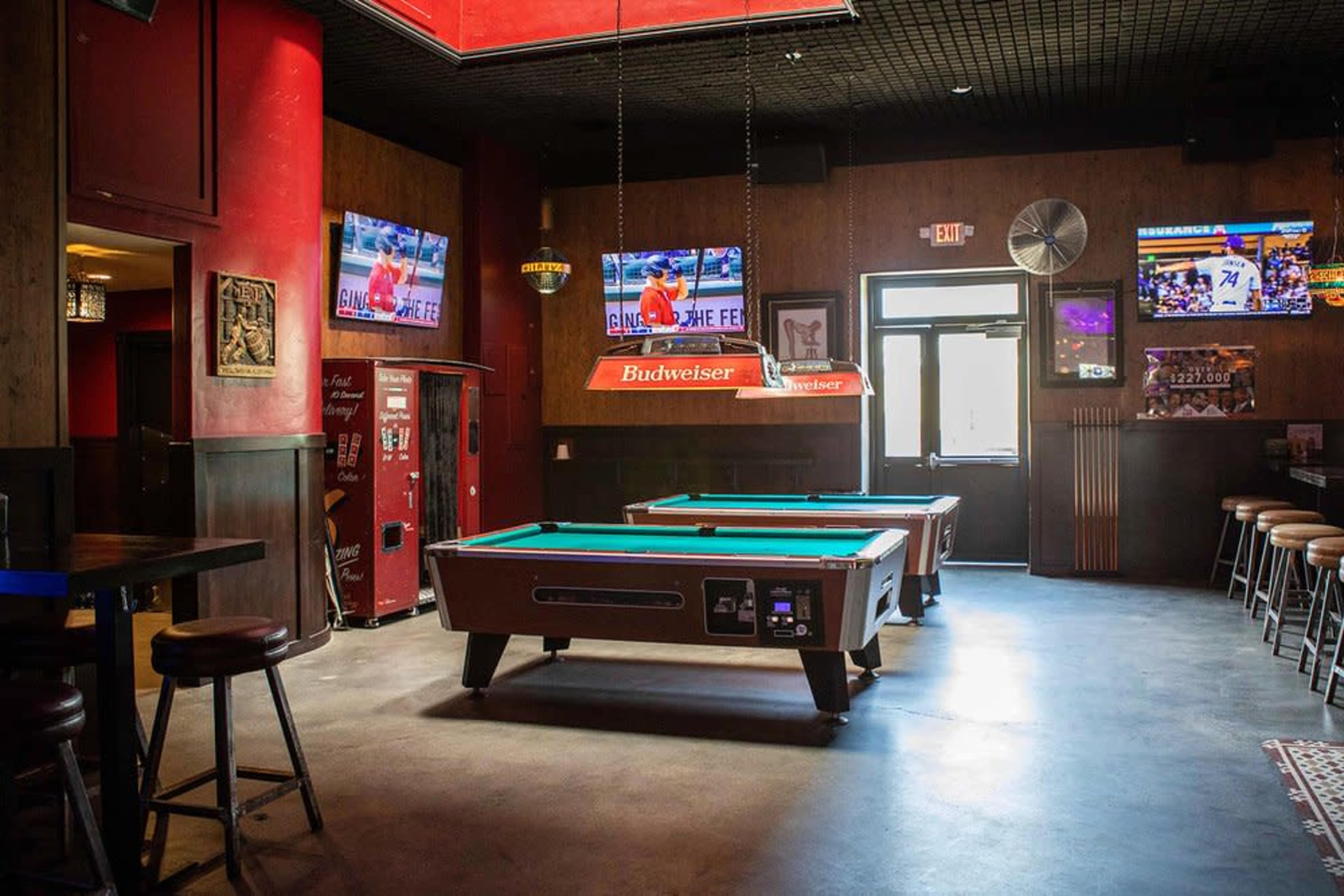 The image shows a bar interior with two pool tables, several television screens displaying sports, and a vintage red vending machine in the corner.