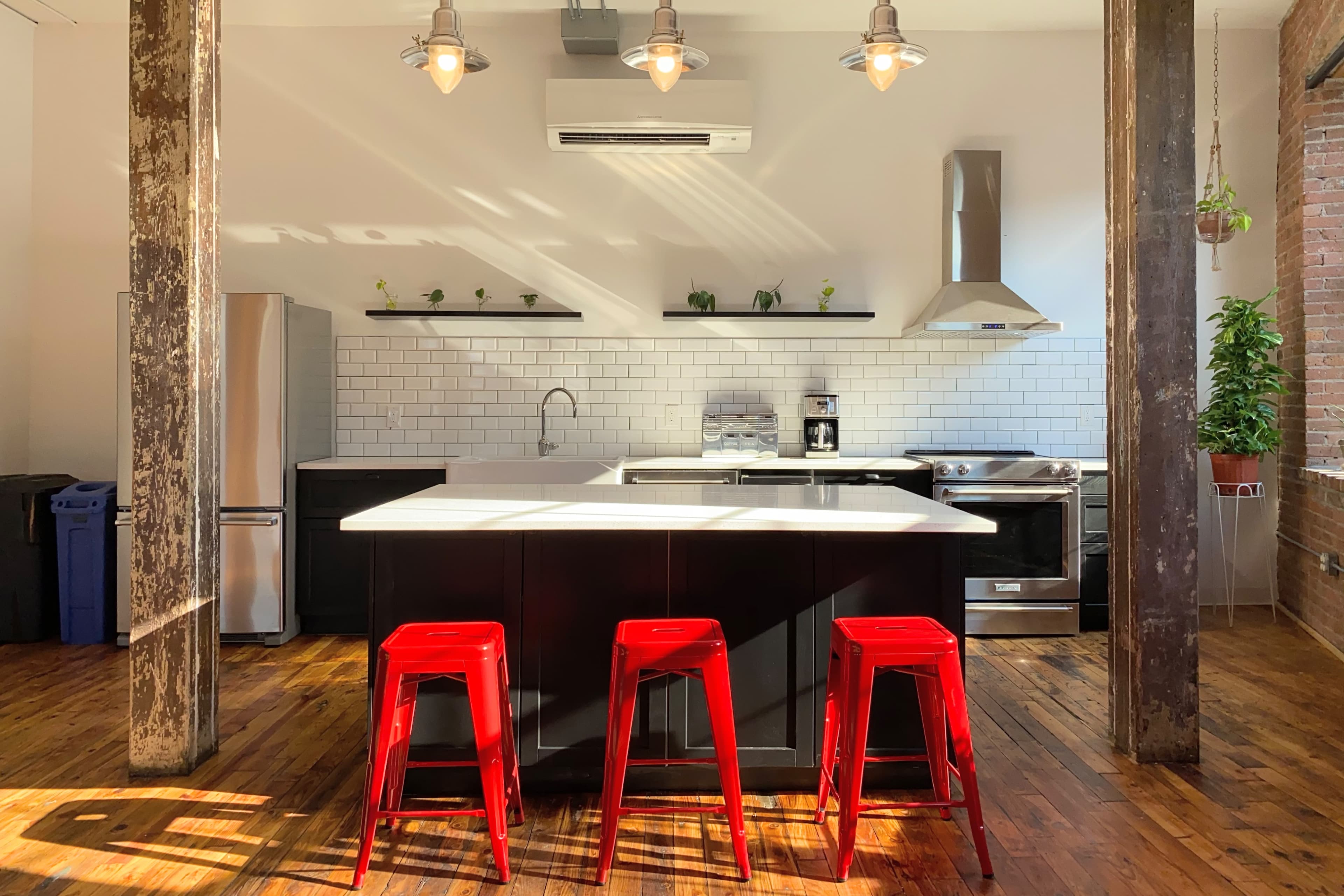 A modern kitchen features a central island with three red stools, stainless steel appliances, and white subway tile backsplash.