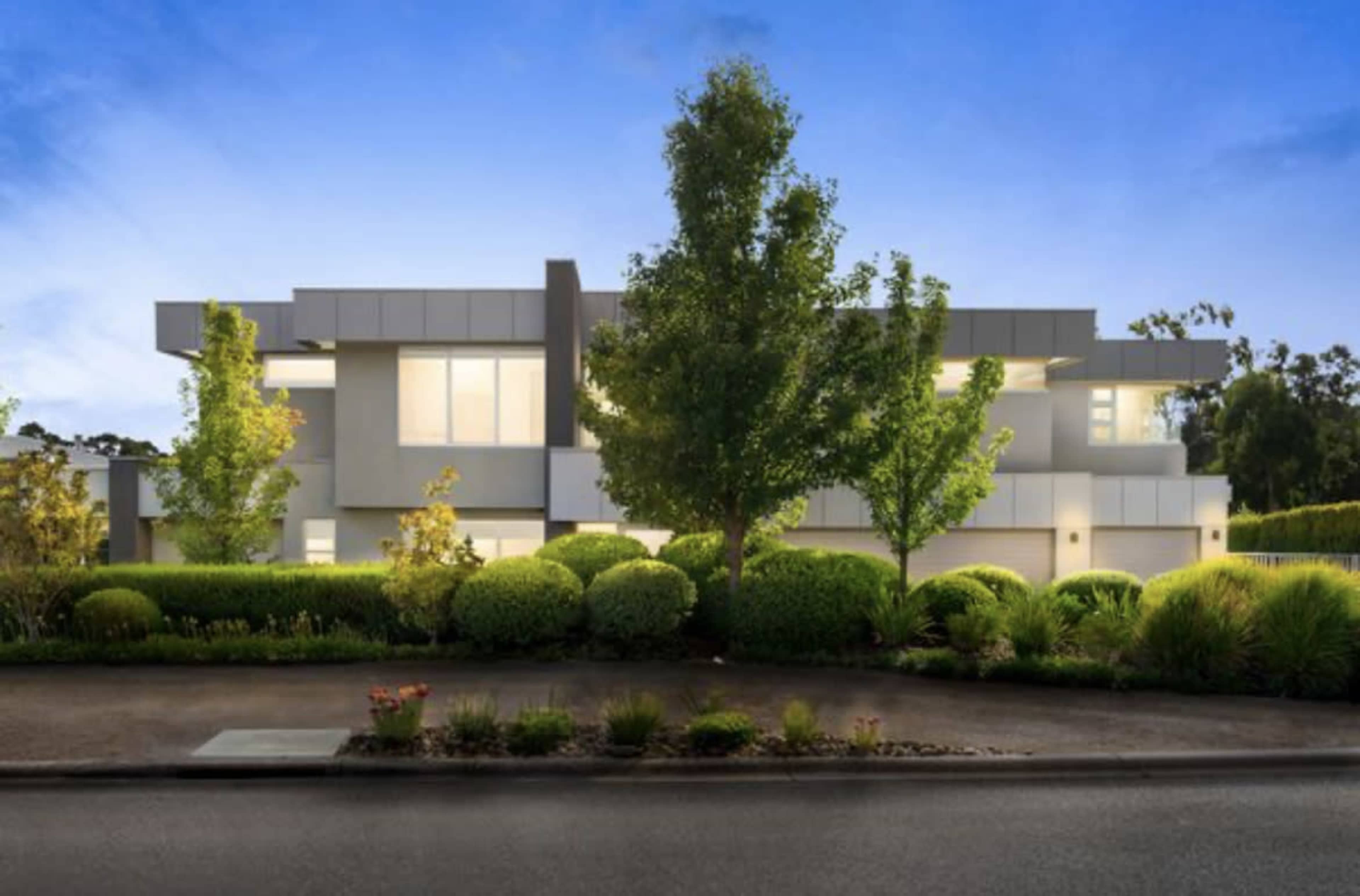 A modern two-story house is surrounded by well-maintained landscaping and trees, with a clear evening sky in the background.