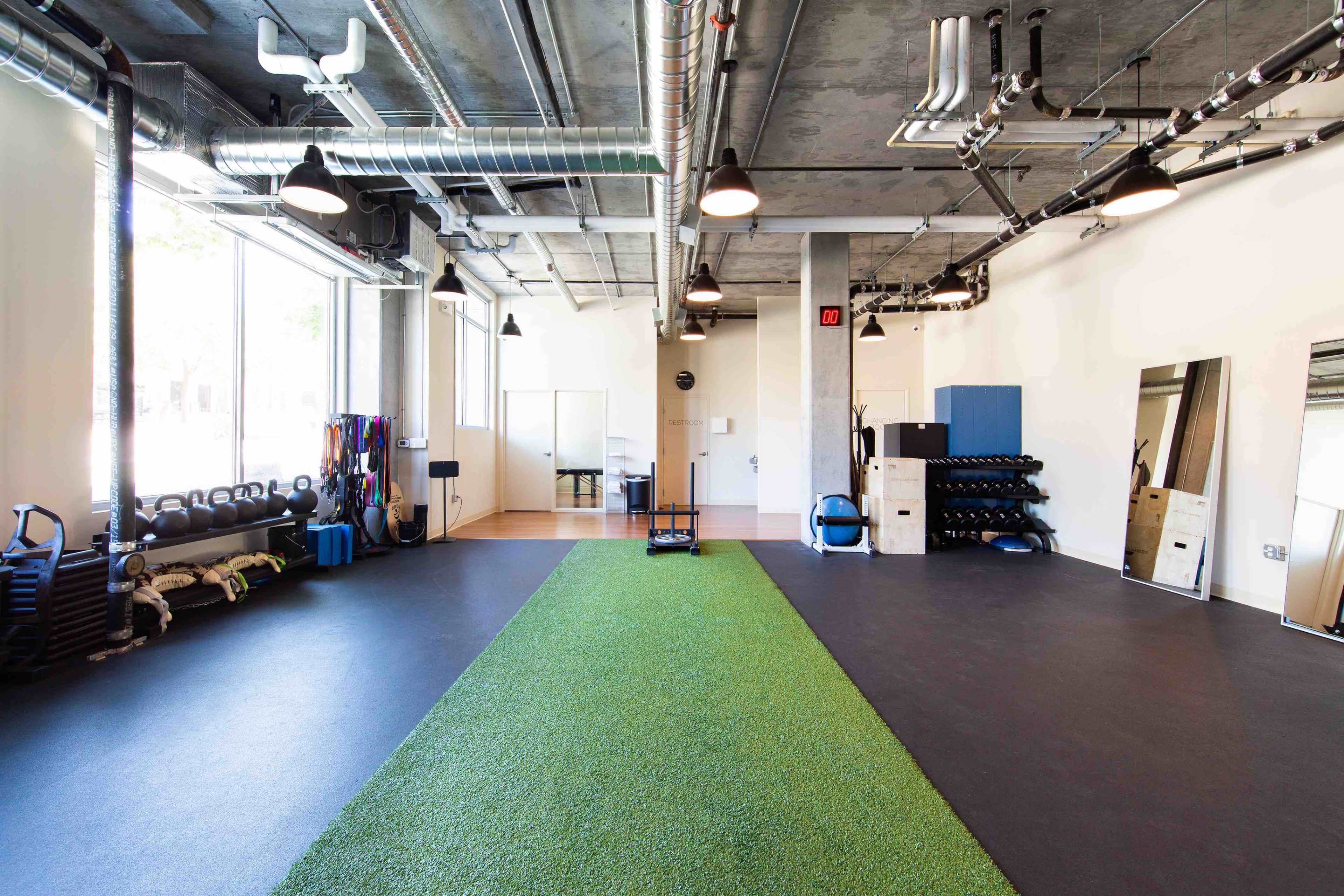 A modern gym space with artificial turf running down the center and various workout equipment arranged along the walls.