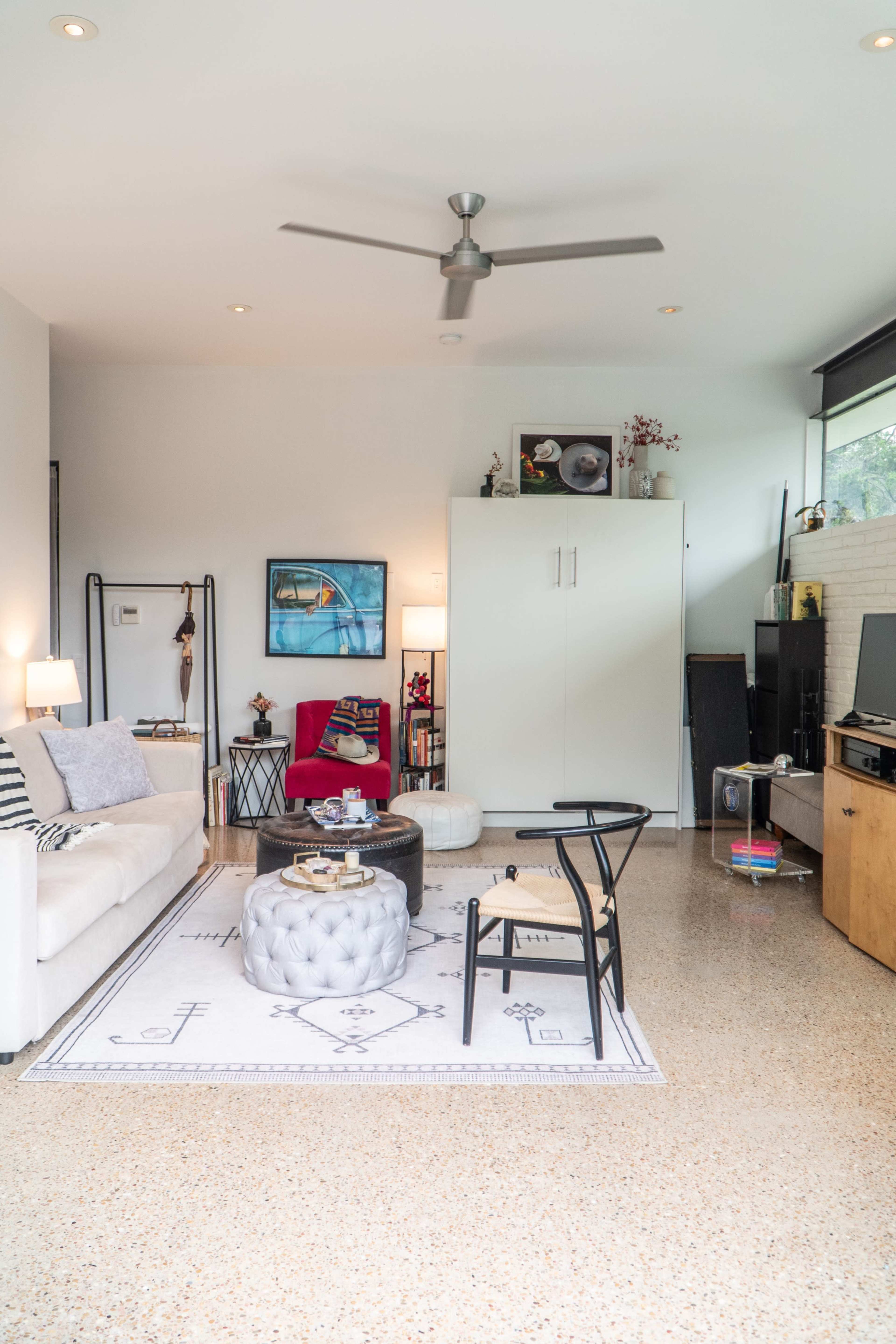 The image shows a modern living room with a white sofa, a round coffee table, a red accent chair, and a large cabinet against the wall.