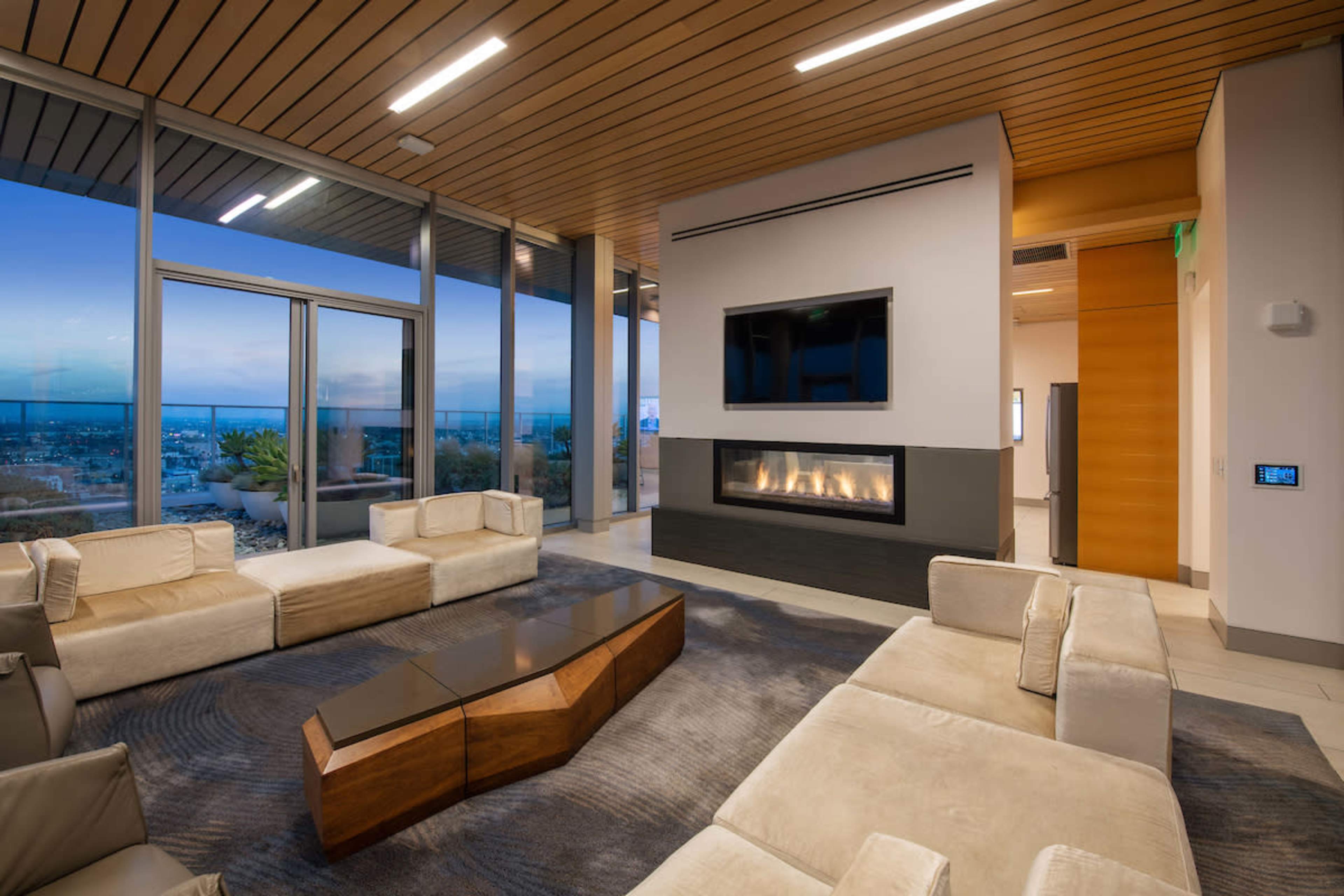 A modern living room features a central coffee table, stylish sofas, a fireplace, and large windows showcasing a scenic view.