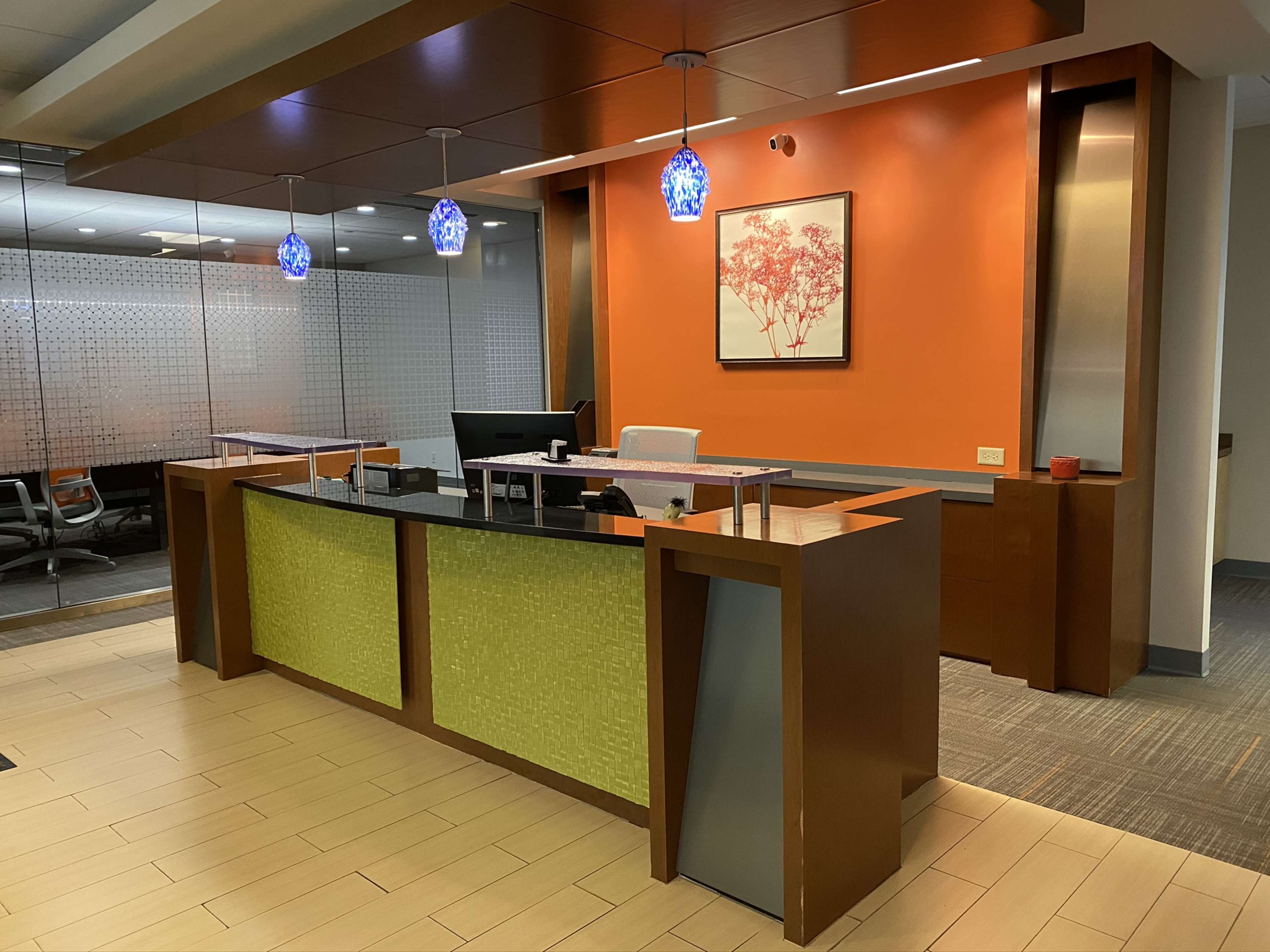A modern reception area featuring a front desk with a green accent panel, orange walls, and pendant lighting.