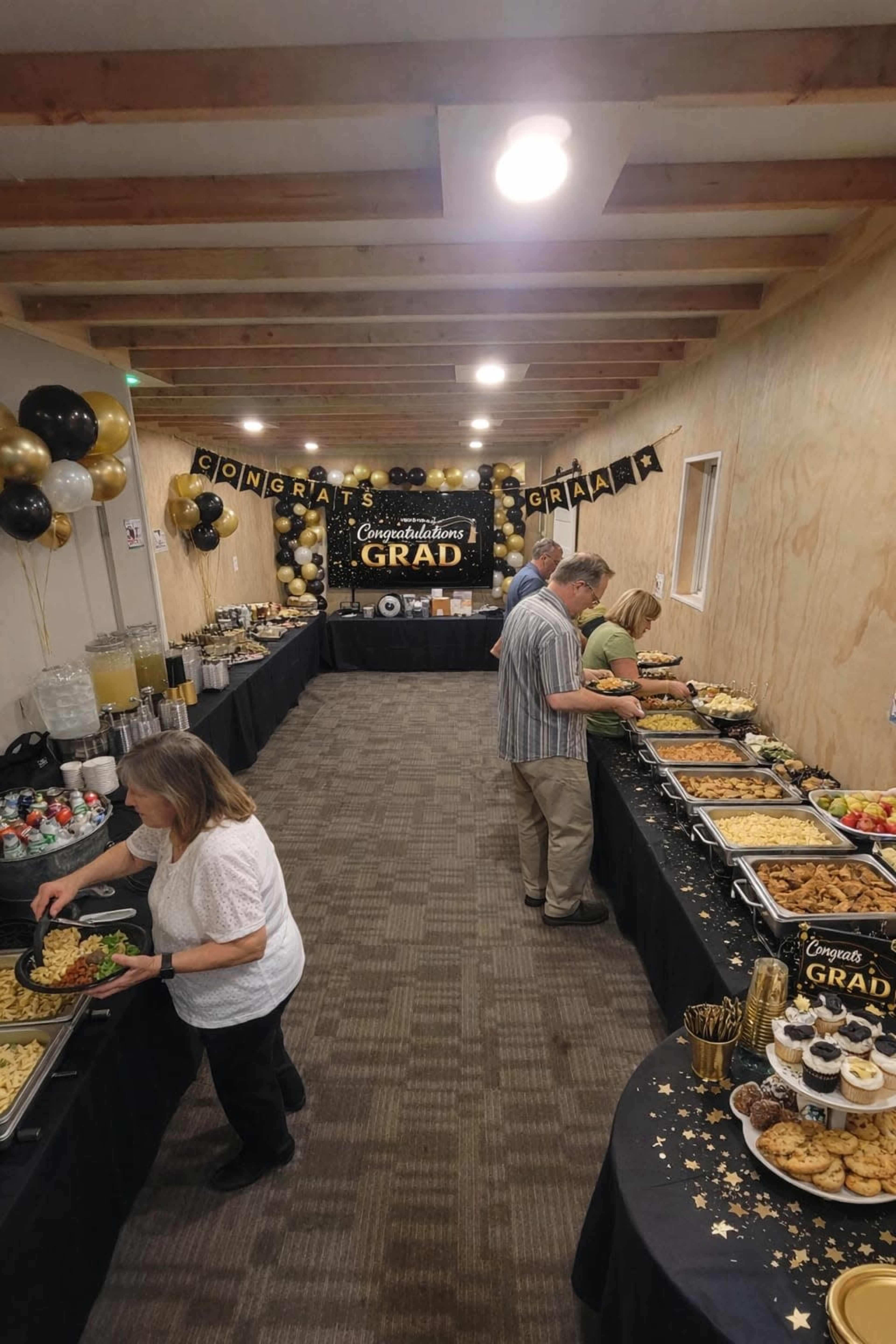 A buffet table is filled with various dishes and desserts as guests serve themselves at a graduation celebration.
