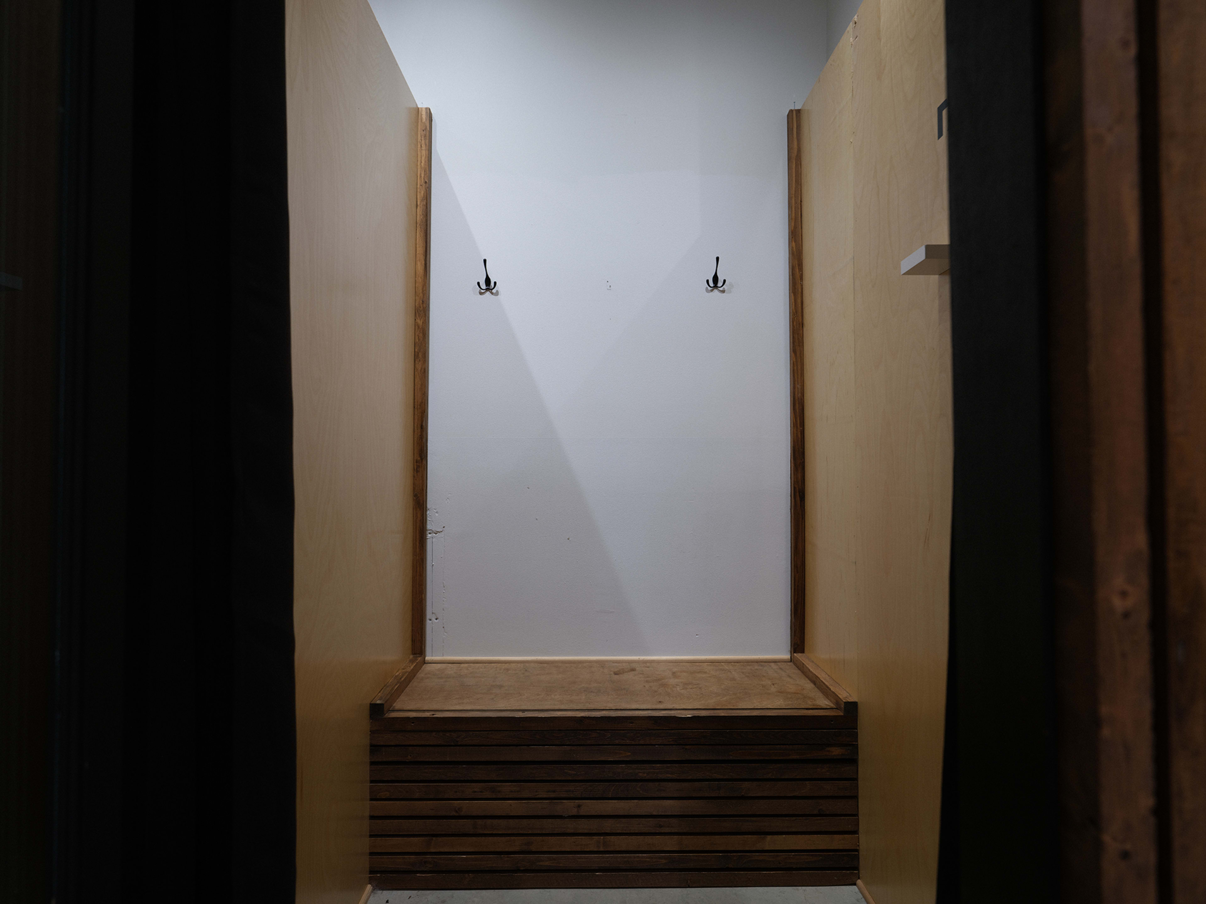 The image shows an empty enclosed space with a wooden bench and two wall-mounted hooks.