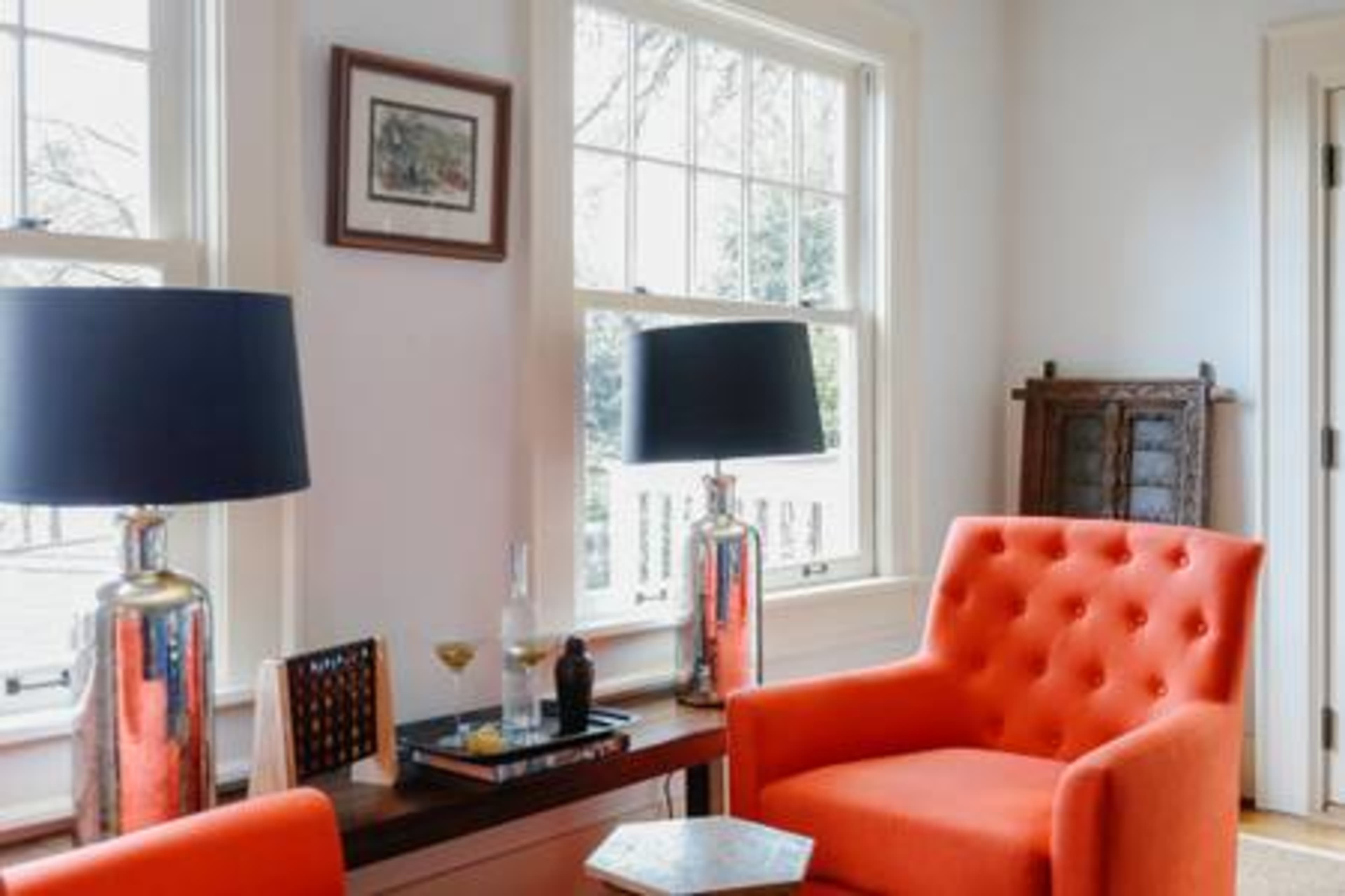 A bright room with two orange armchairs, a wooden table with decorative items, and two lamps on either side.