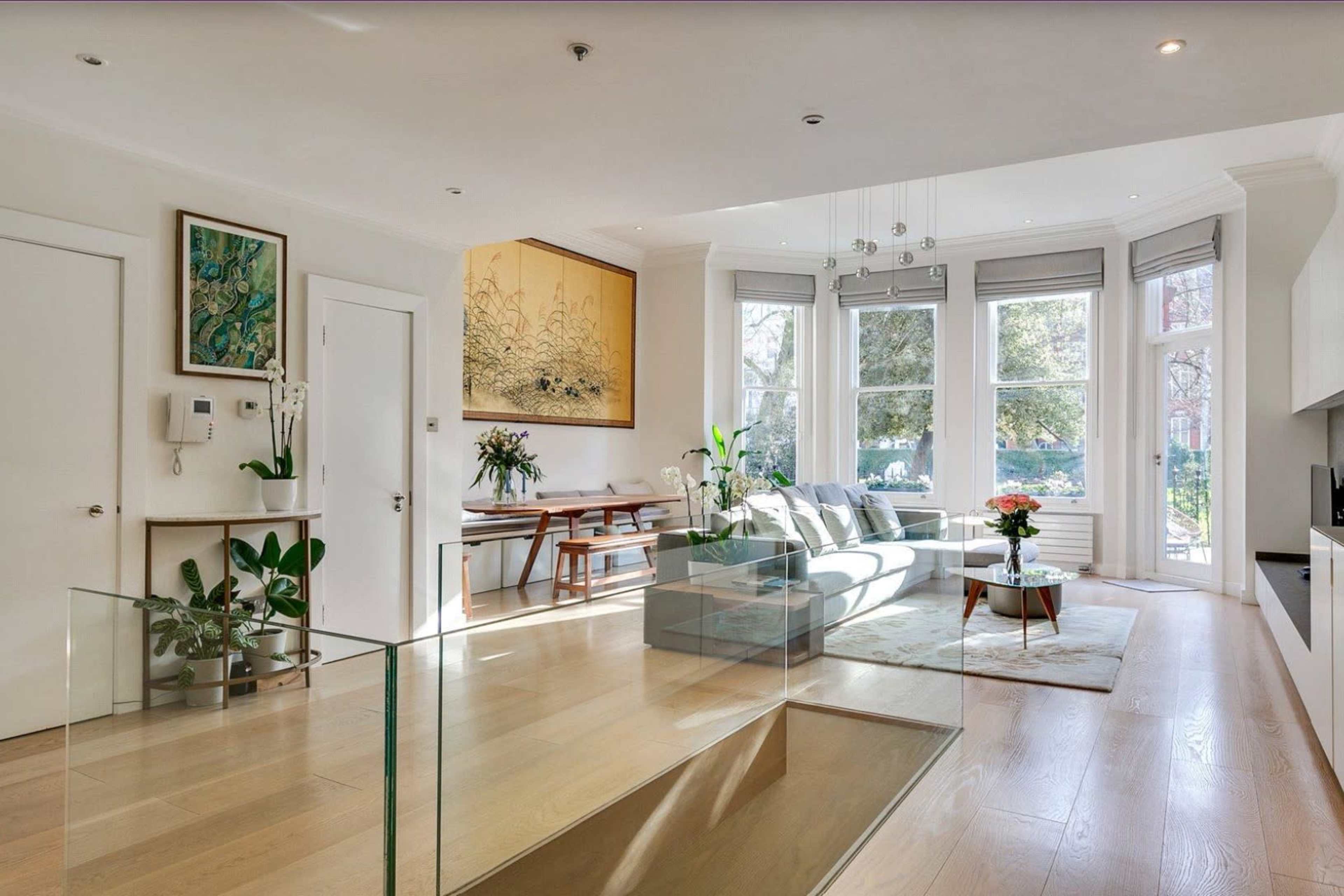 A bright, modern living room with a glass railing, contemporary furniture, and large windows allowing natural light to fill the space.