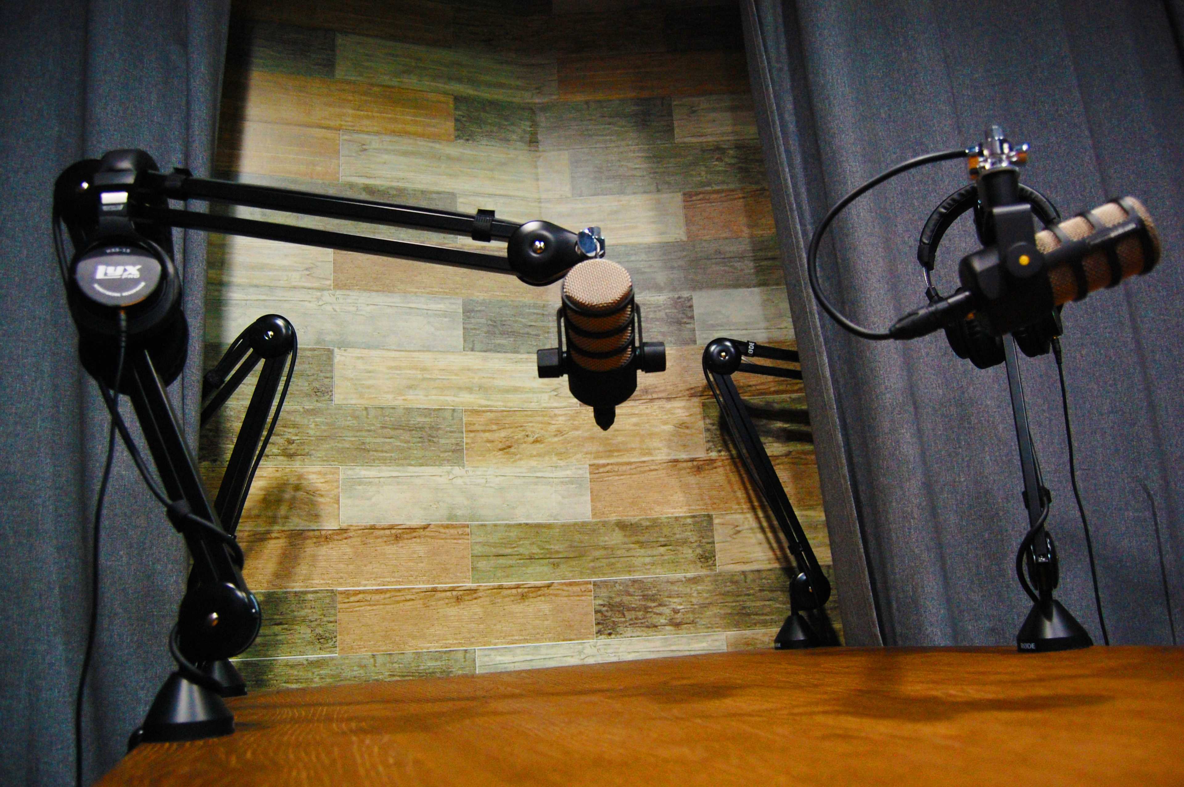 Two microphones are mounted on adjustable arms facing a wooden table in a room with a textured wall.