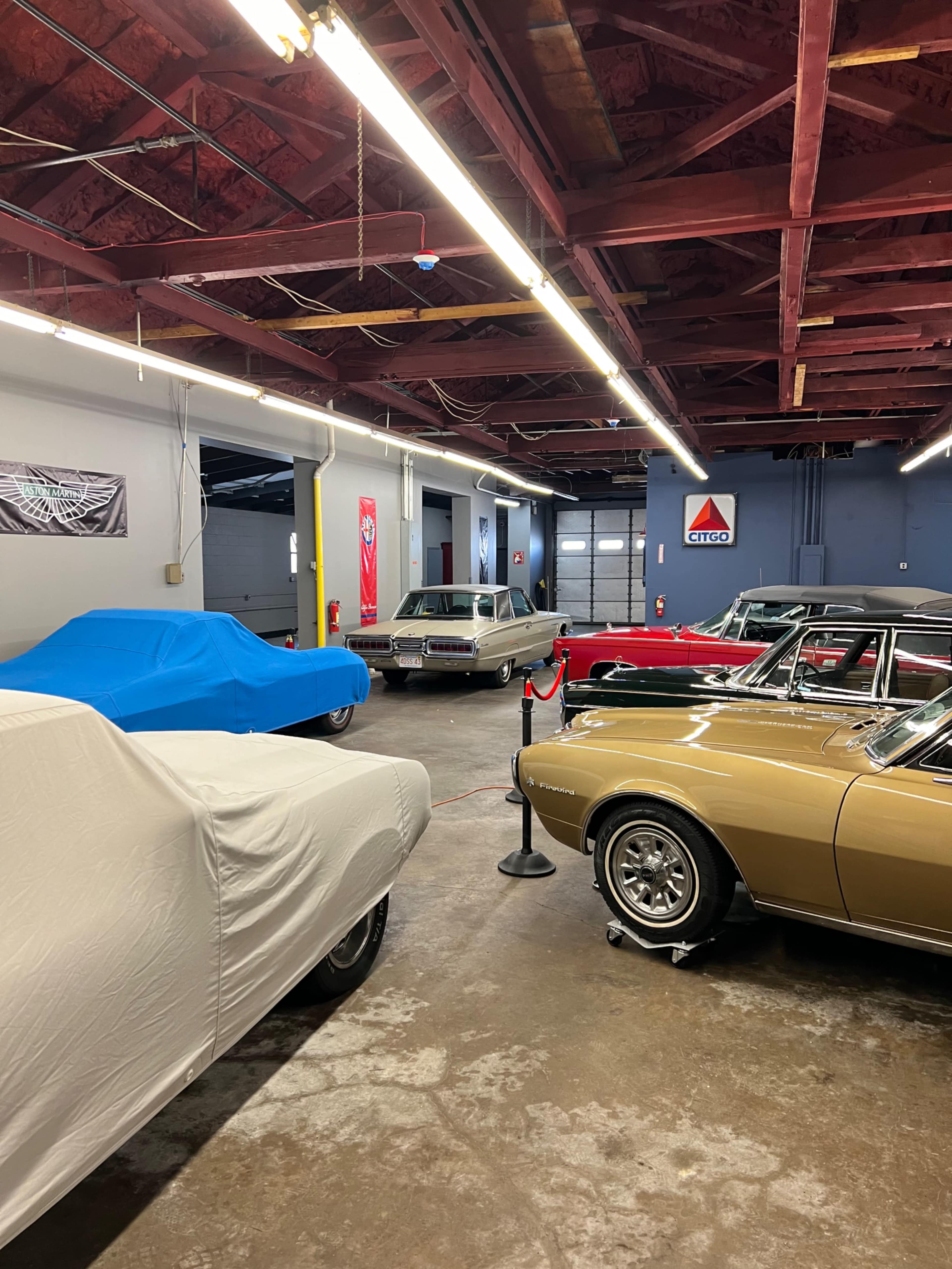 A collection of vintage cars in a garage, with some covered and others on display.