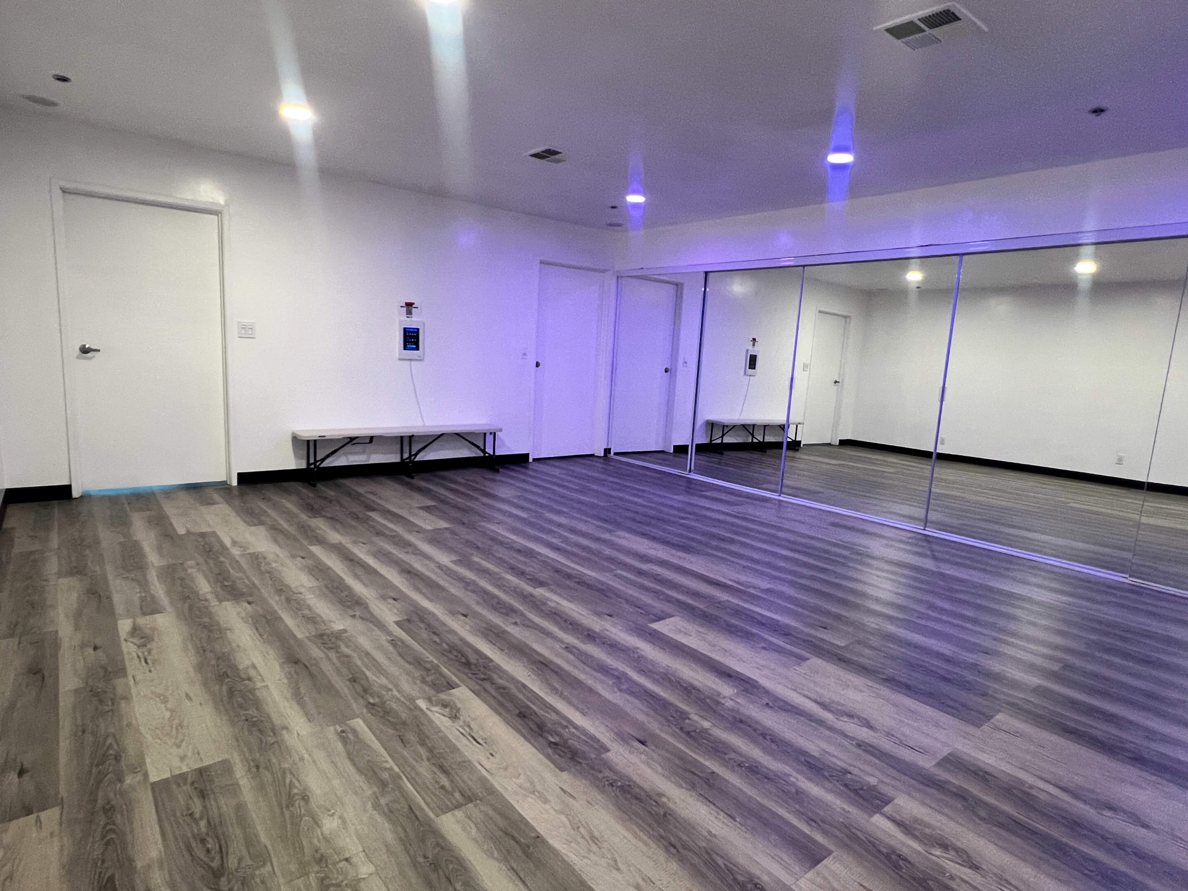 The image shows a spacious, well-lit room with large mirrors, a bench along one wall, and modern flooring.