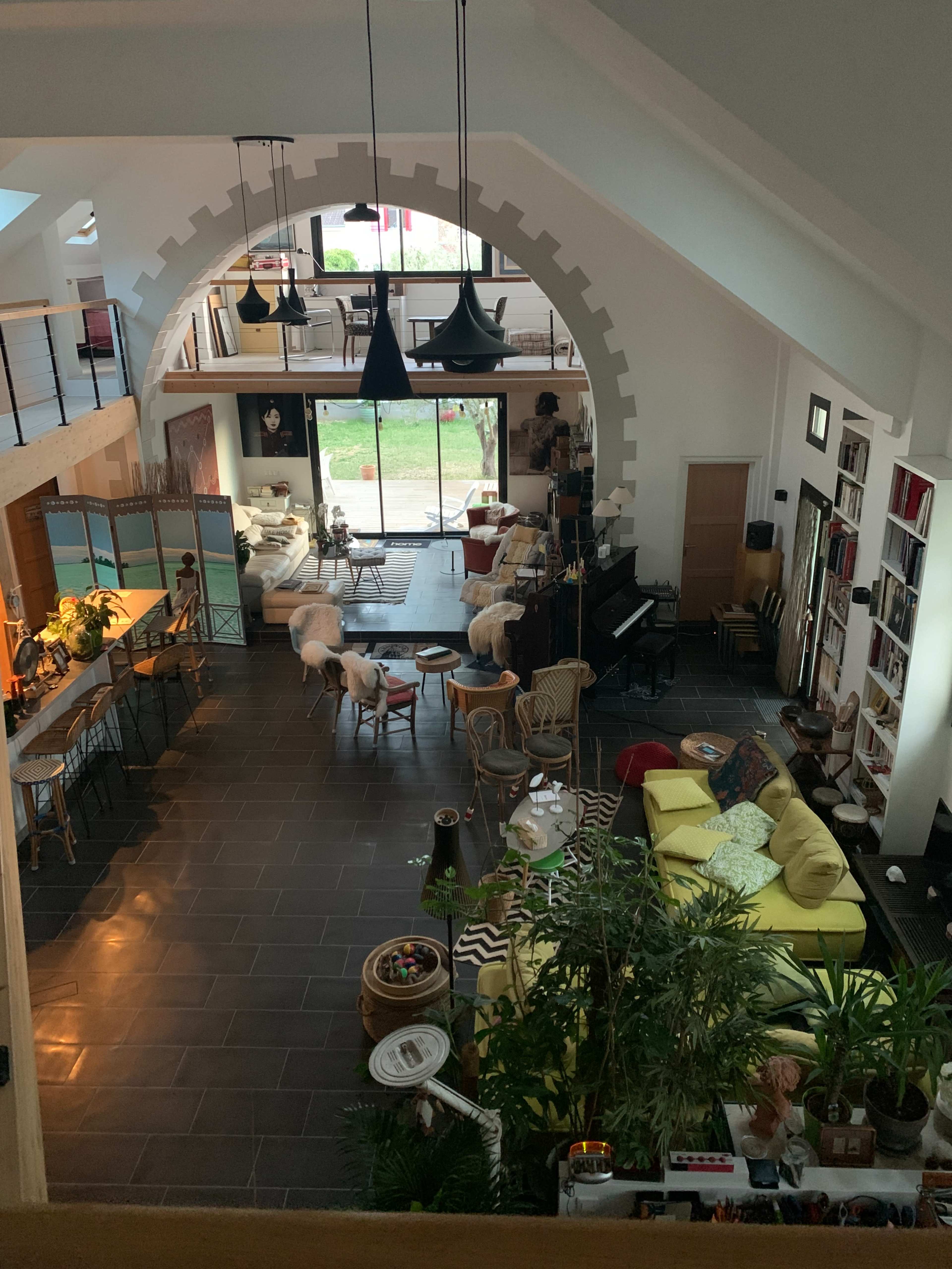 A spacious, open-concept living area with various seating arrangements, plants, and large windows letting in natural light.