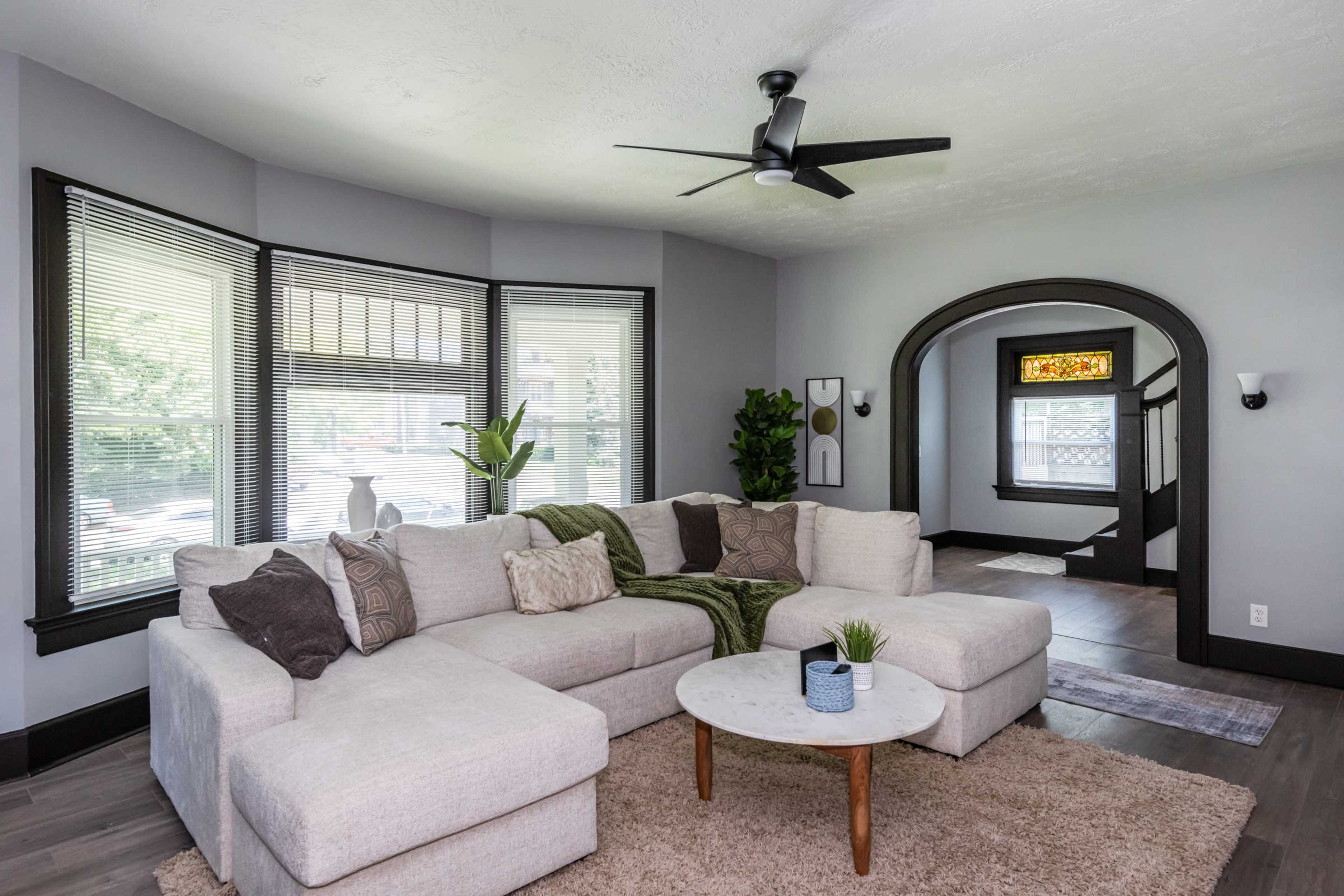 An open living room features a large sectional sofa, a round coffee table, and large windows with natural light.