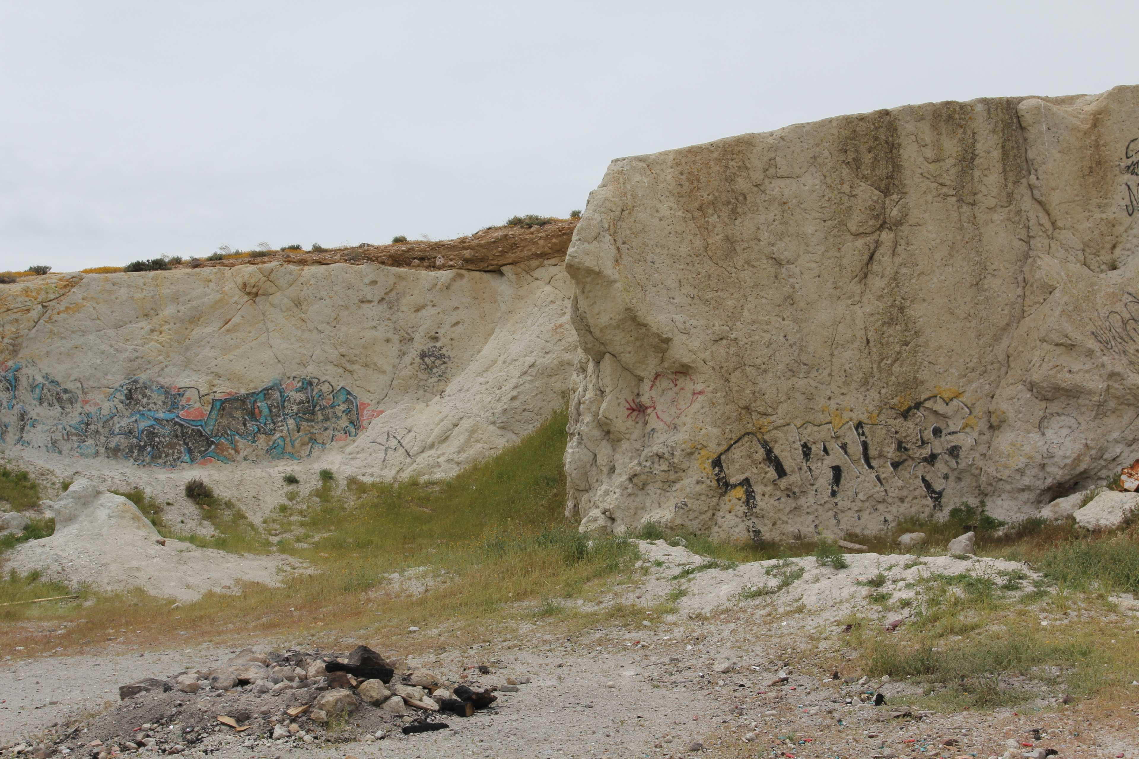 A rocky landscape with large, graffiti-covered cliffs and sparse grass.