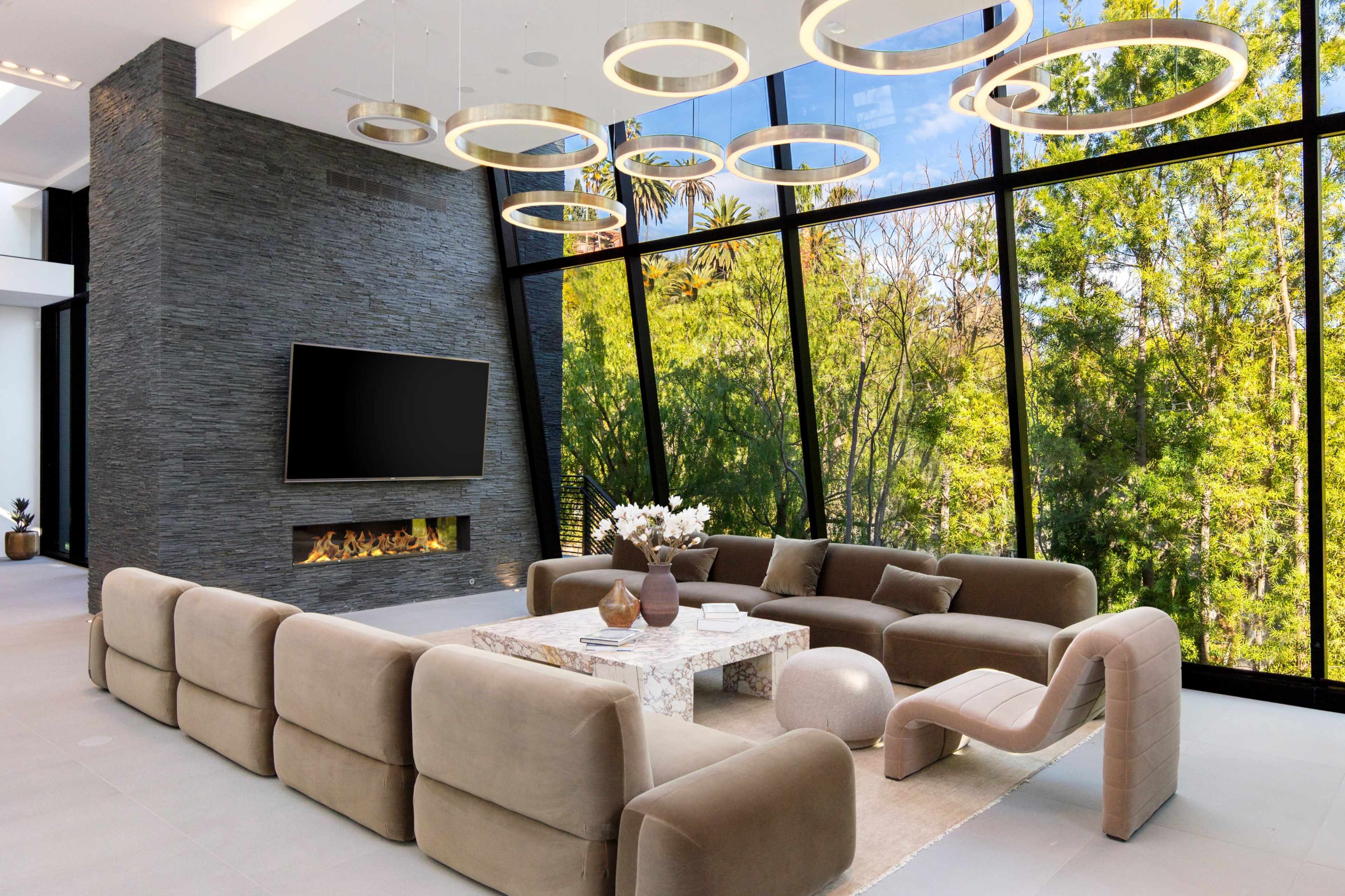 The image features a modern living room with a large sectional sofa, a marble coffee table, and floor-to-ceiling windows overlooking greenery, accented by circular light fixtures.