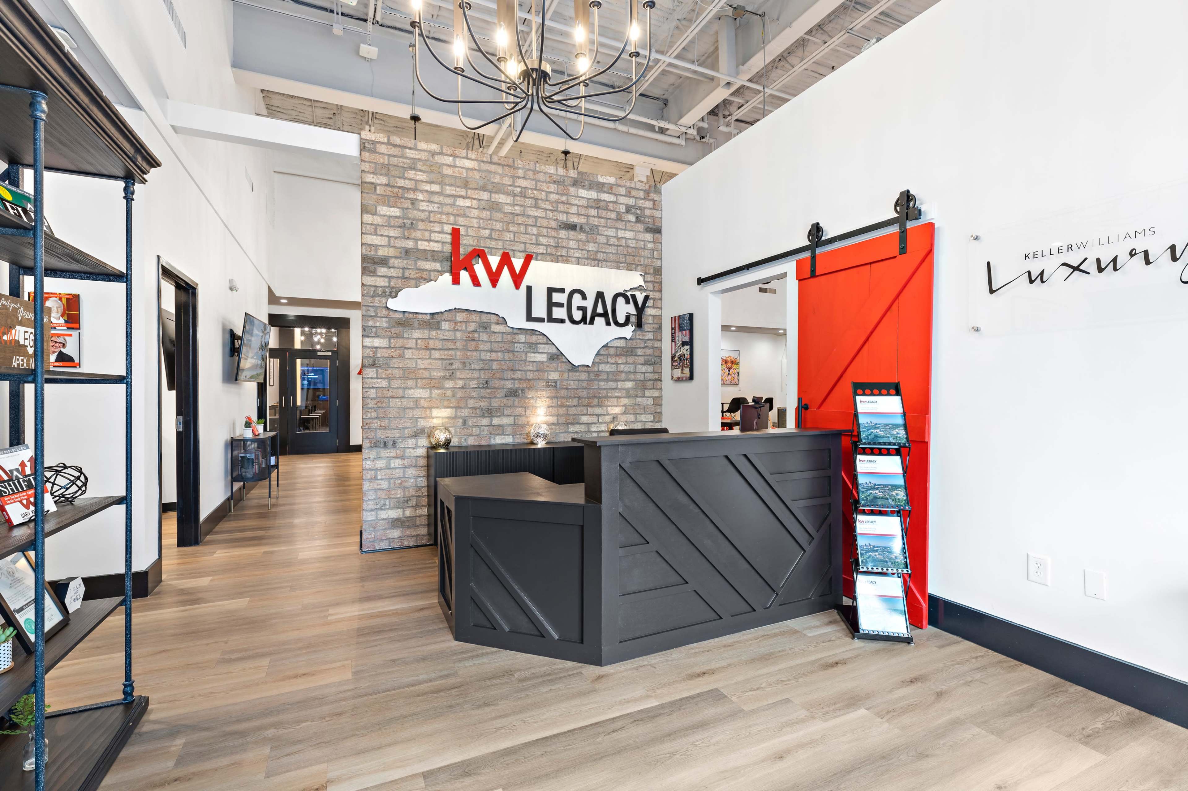 A modern reception area with a brick wall featuring a large logo for "KW Legacy" and a dark wooden reception desk.