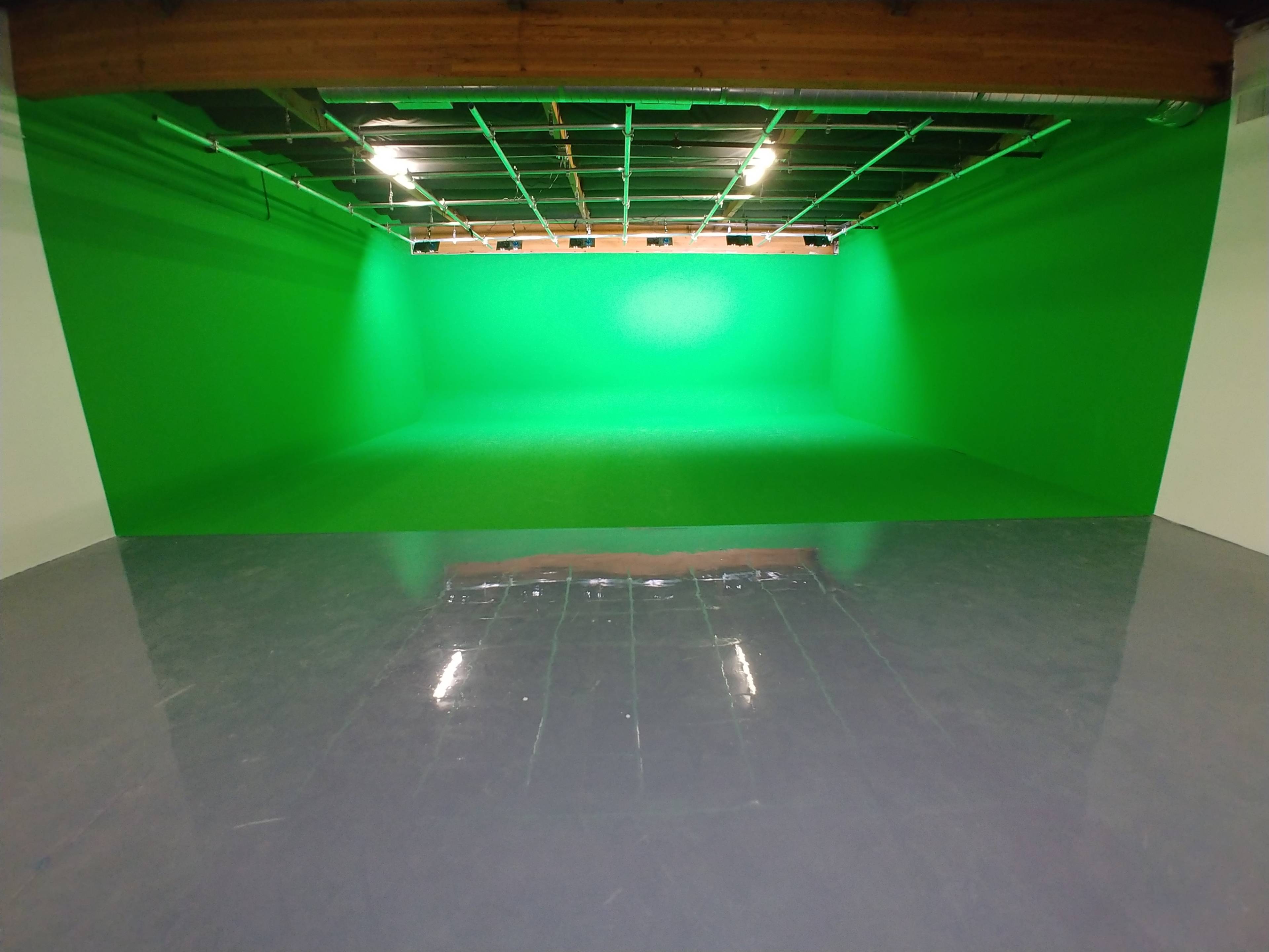 The image shows a spacious room with a bright green screen wall and a shiny gray floor.