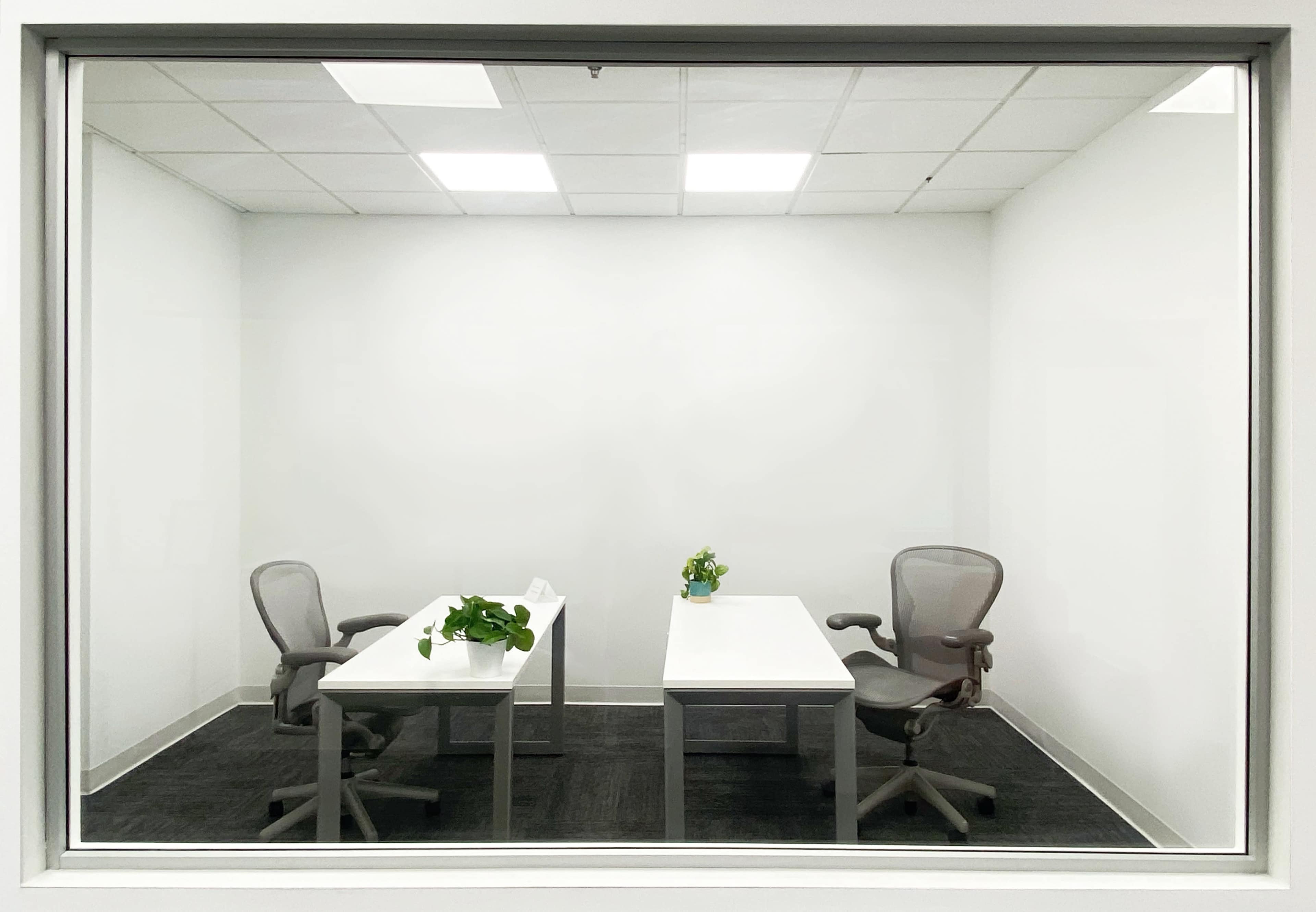 A minimalistic office space with two desks and chairs, separated by a glass wall.