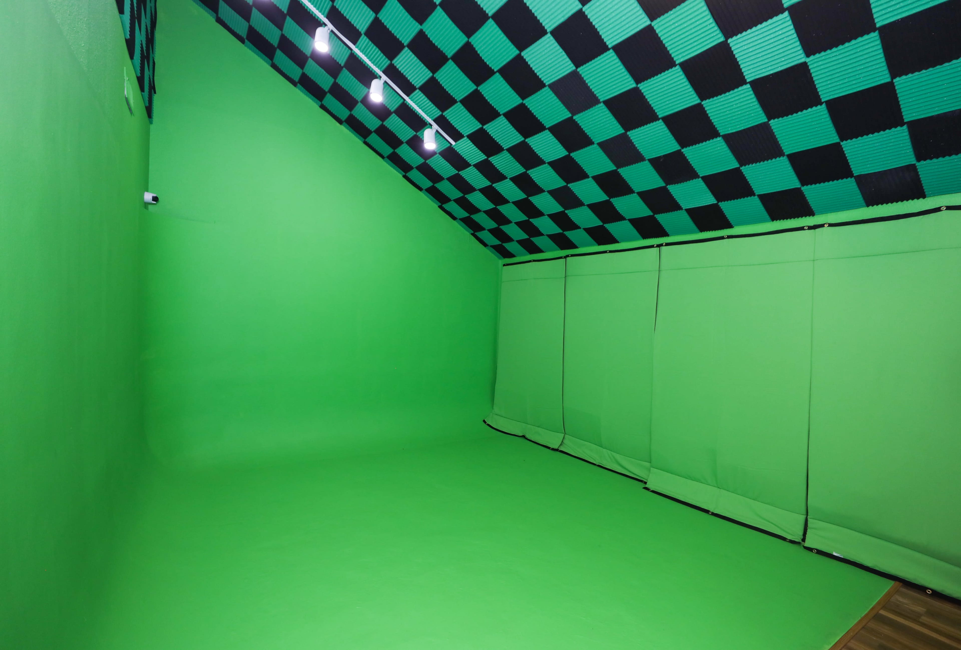 The image shows a green screen studio with a black and green checkered ceiling and smooth green walls and floor.