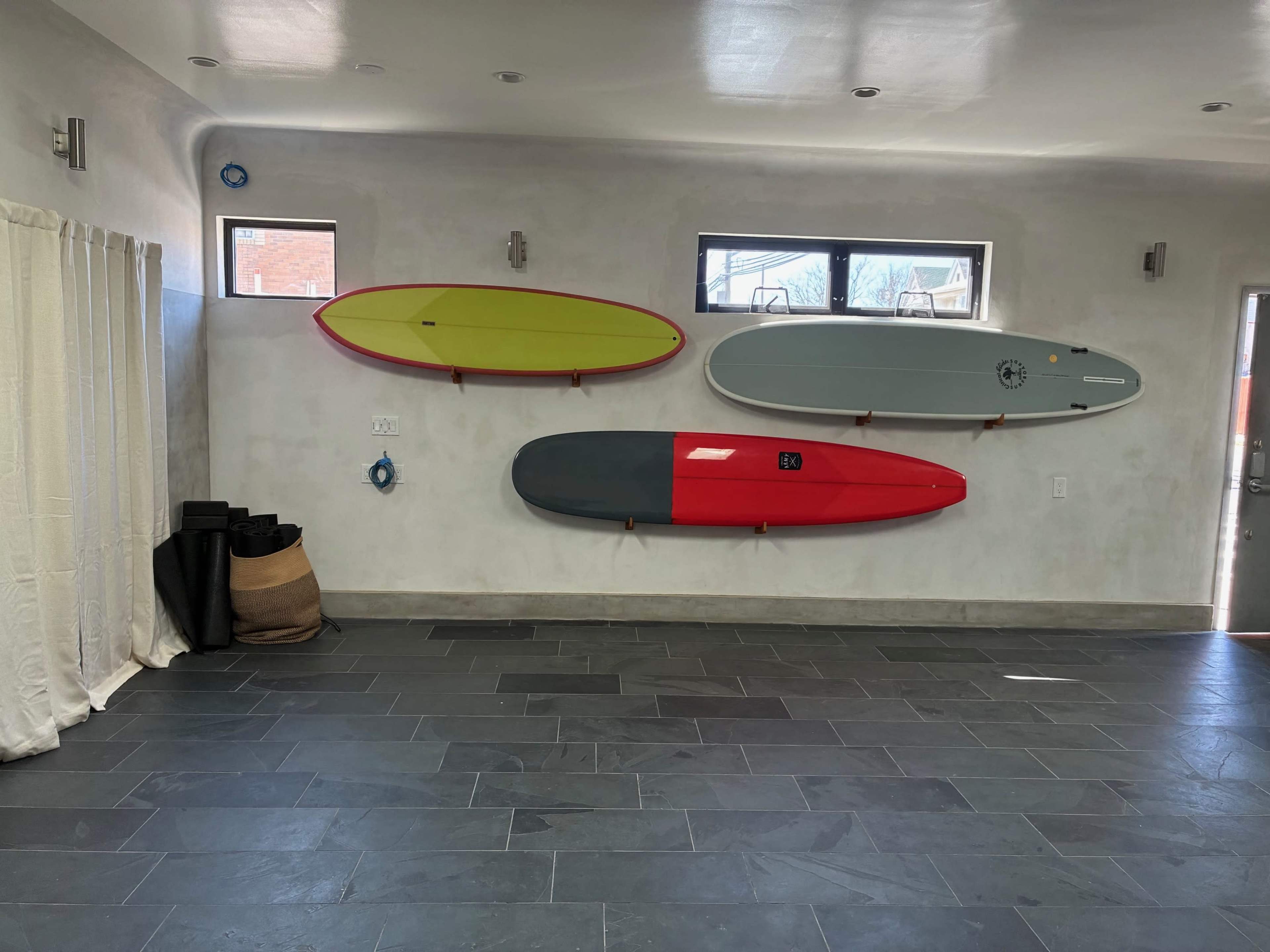 The image shows a room with a smooth gray wall displaying three surfboards in bright colors, along with a textured floor and a curtain to the left.