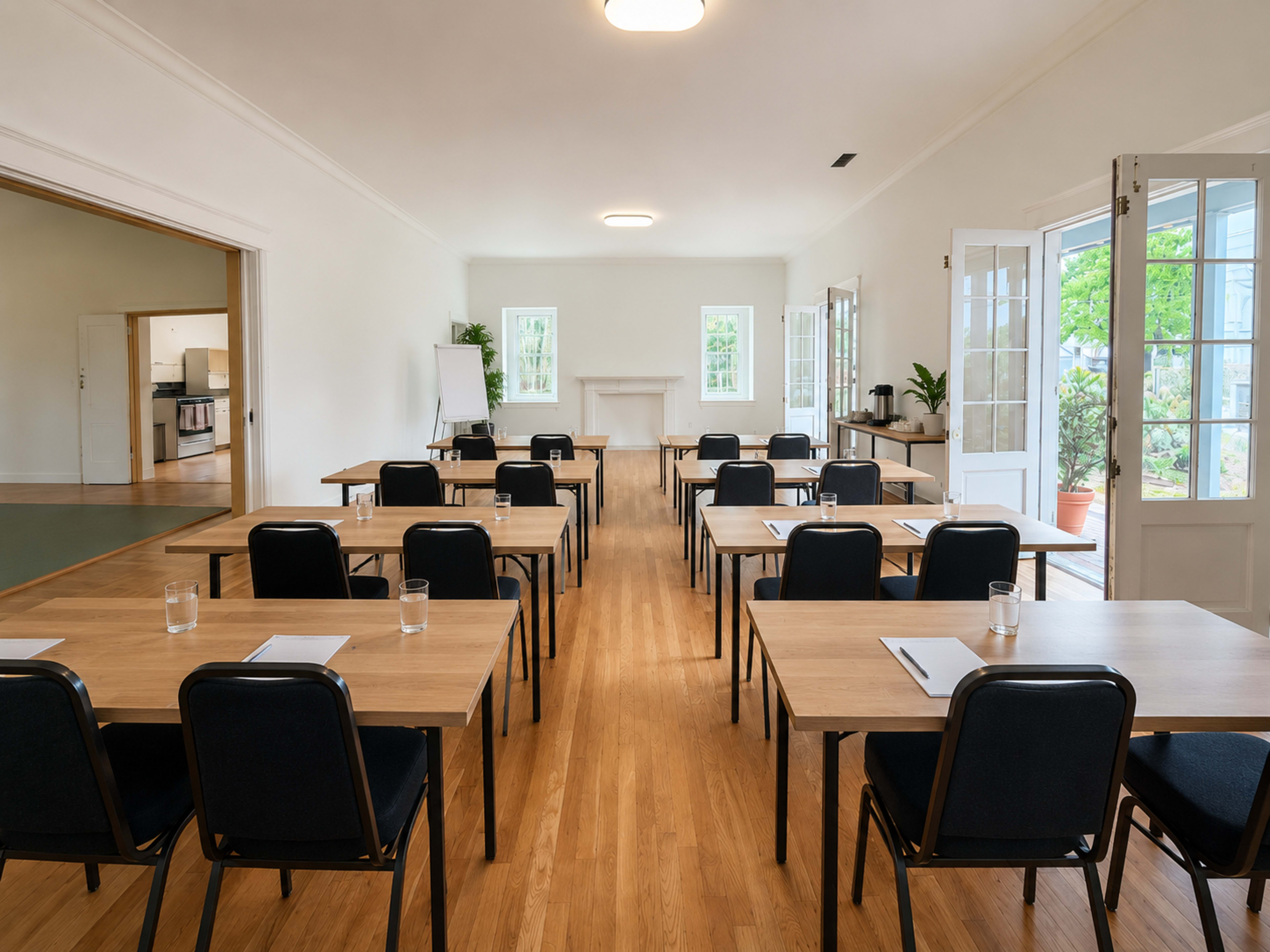 The image shows a bright, empty classroom set up with several rows of tables and chairs facing the front, where a fireplace and windows are visible.