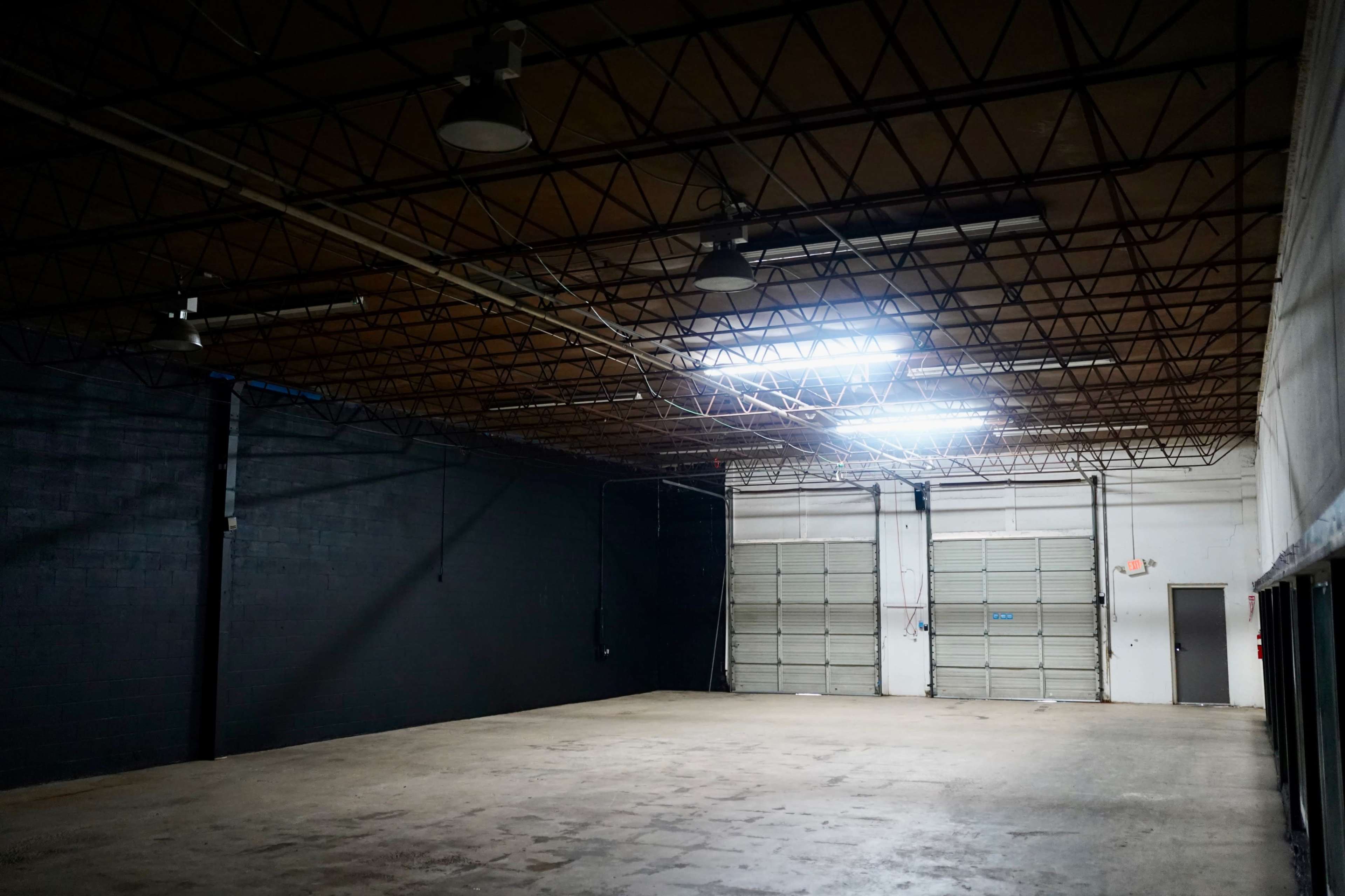 The image shows a large, empty industrial space with a high ceiling and minimal illumination from overhead lights.