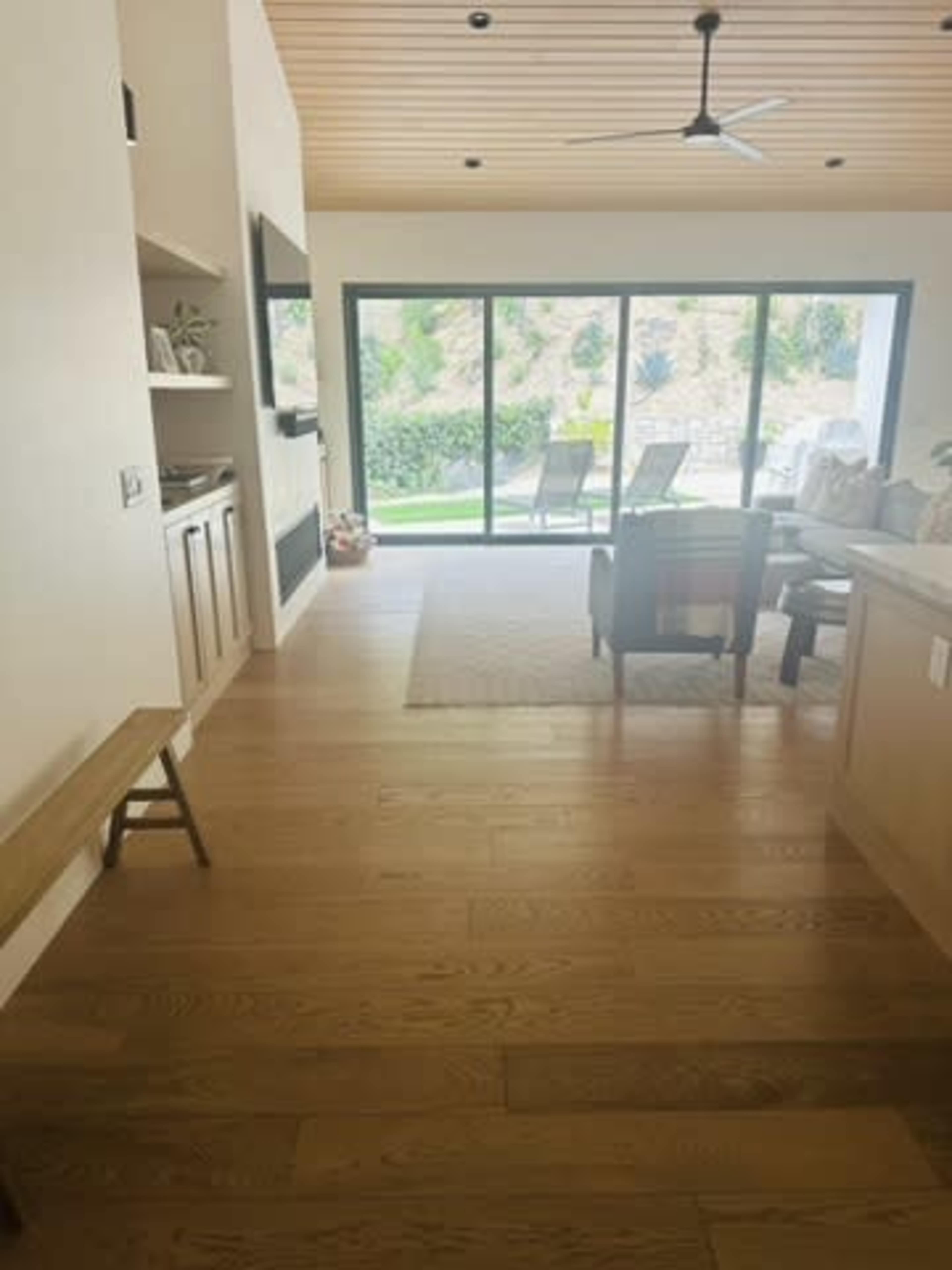 The image shows a spacious living area with wooden flooring, featuring large windows that open to a landscaped outdoor space.