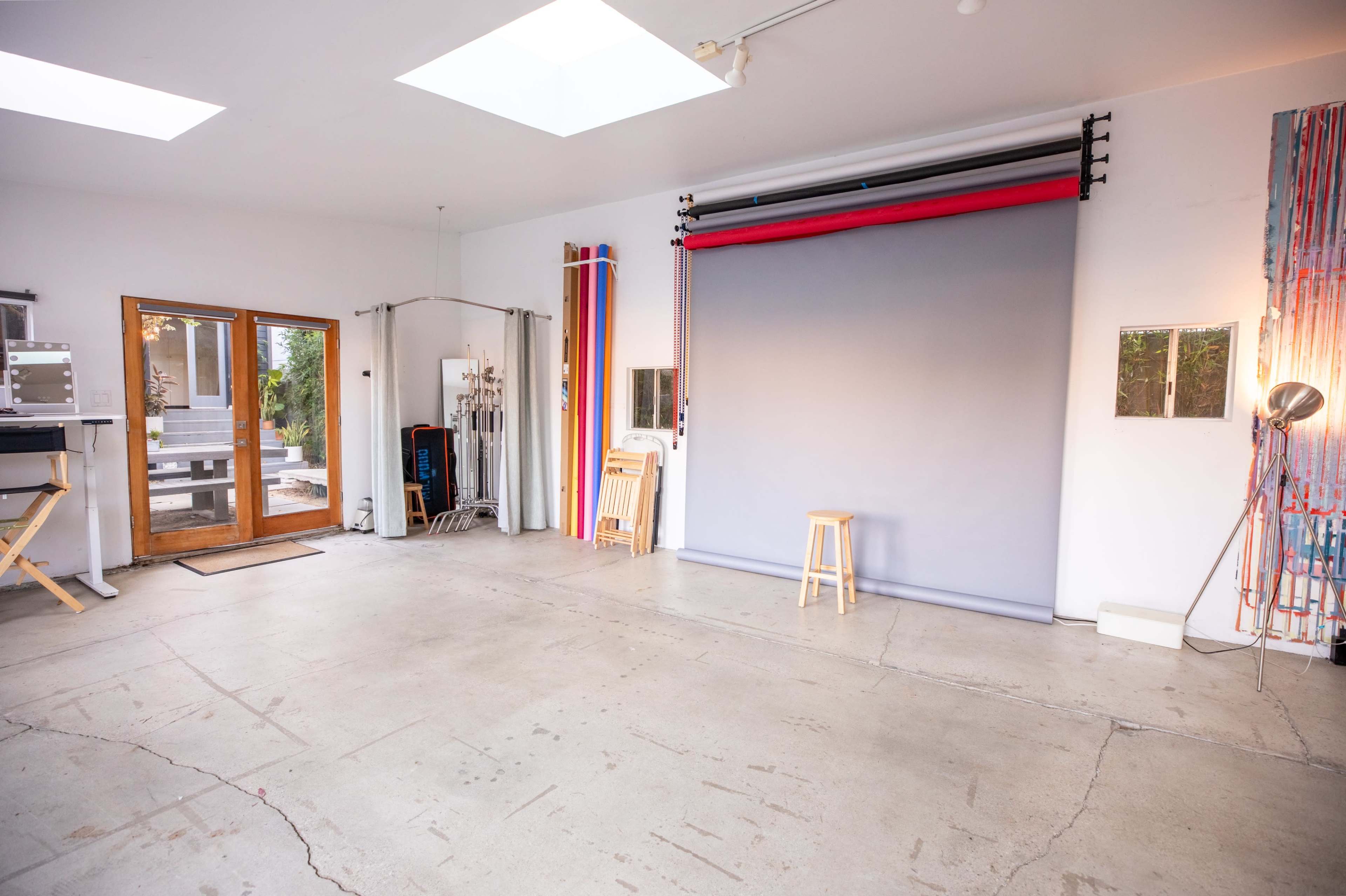 A spacious studio with a gray backdrop, a wooden stool in the center, and various photography equipment along the walls.
