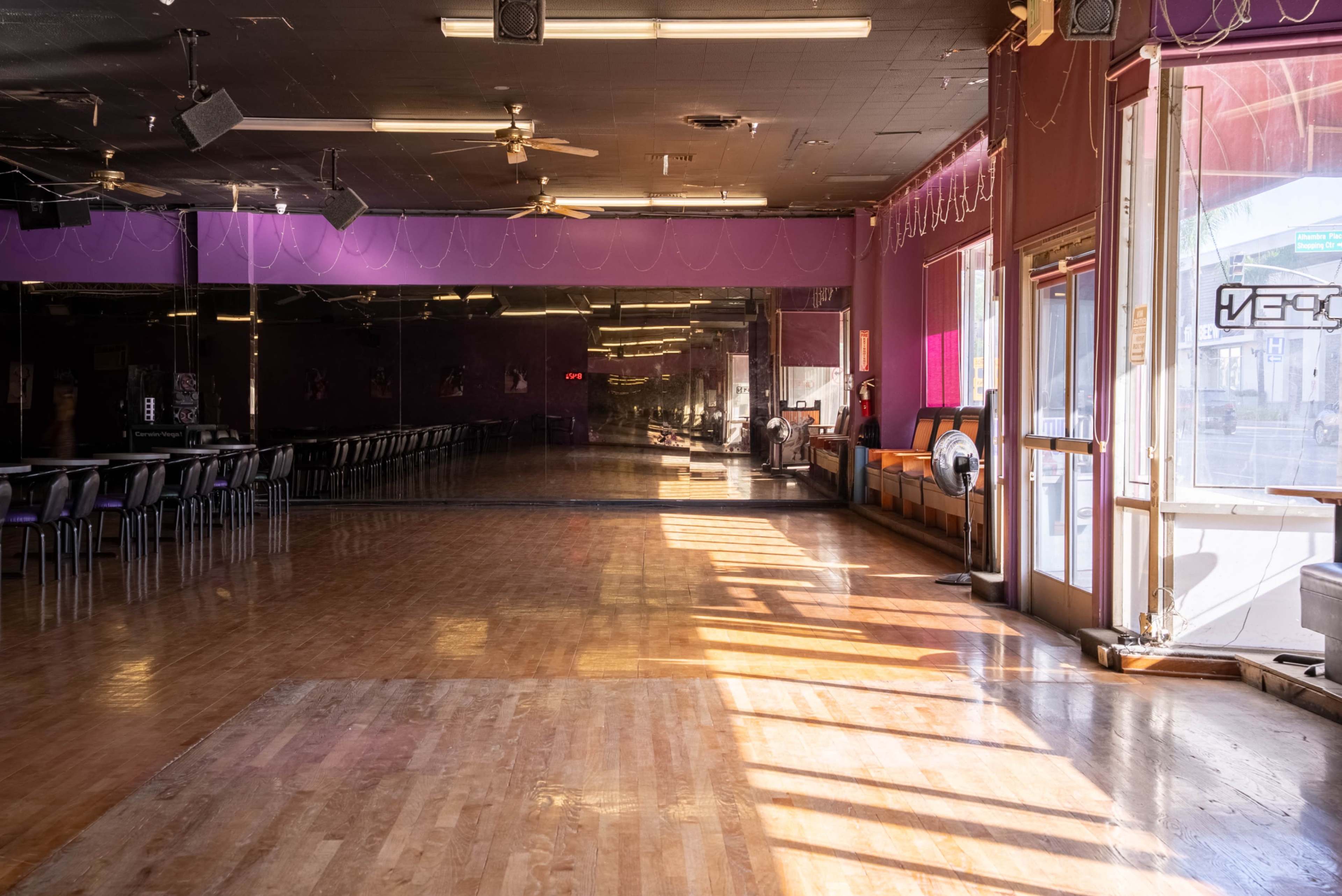 The image shows an empty dance studio with wooden floors, large mirrors on one wall, and sunlight streaming through windows.