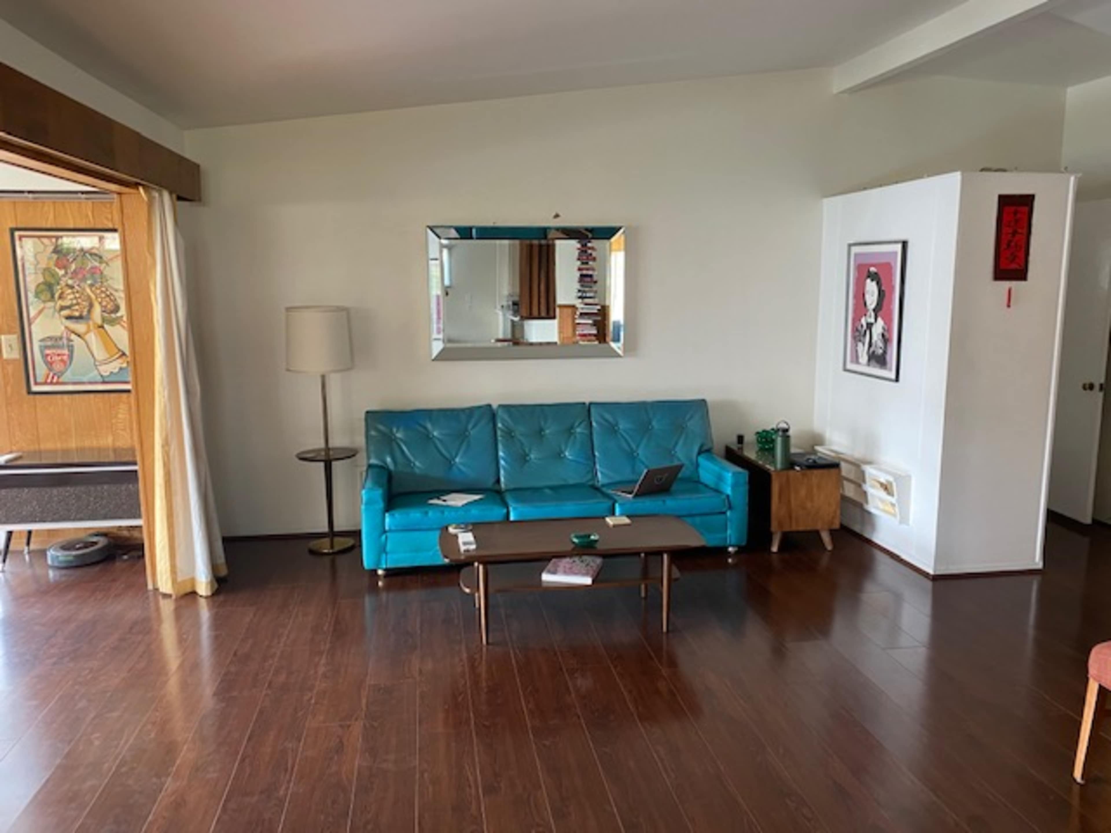 A modern living room with a turquoise sofa, a wooden coffee table, a floor lamp, and a mirror on the wall.