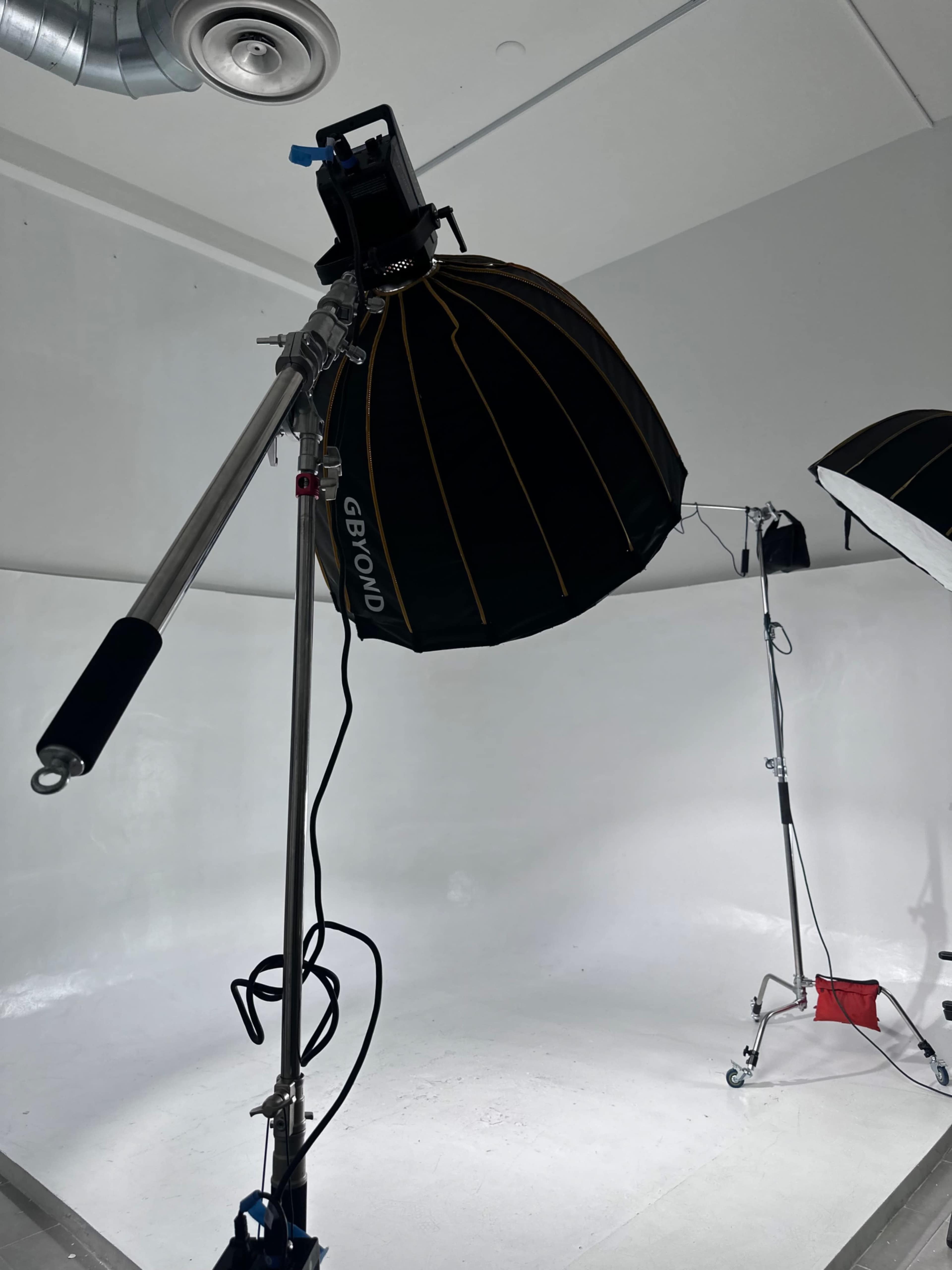 The image shows a photography studio with lighting equipment set up against a white backdrop.