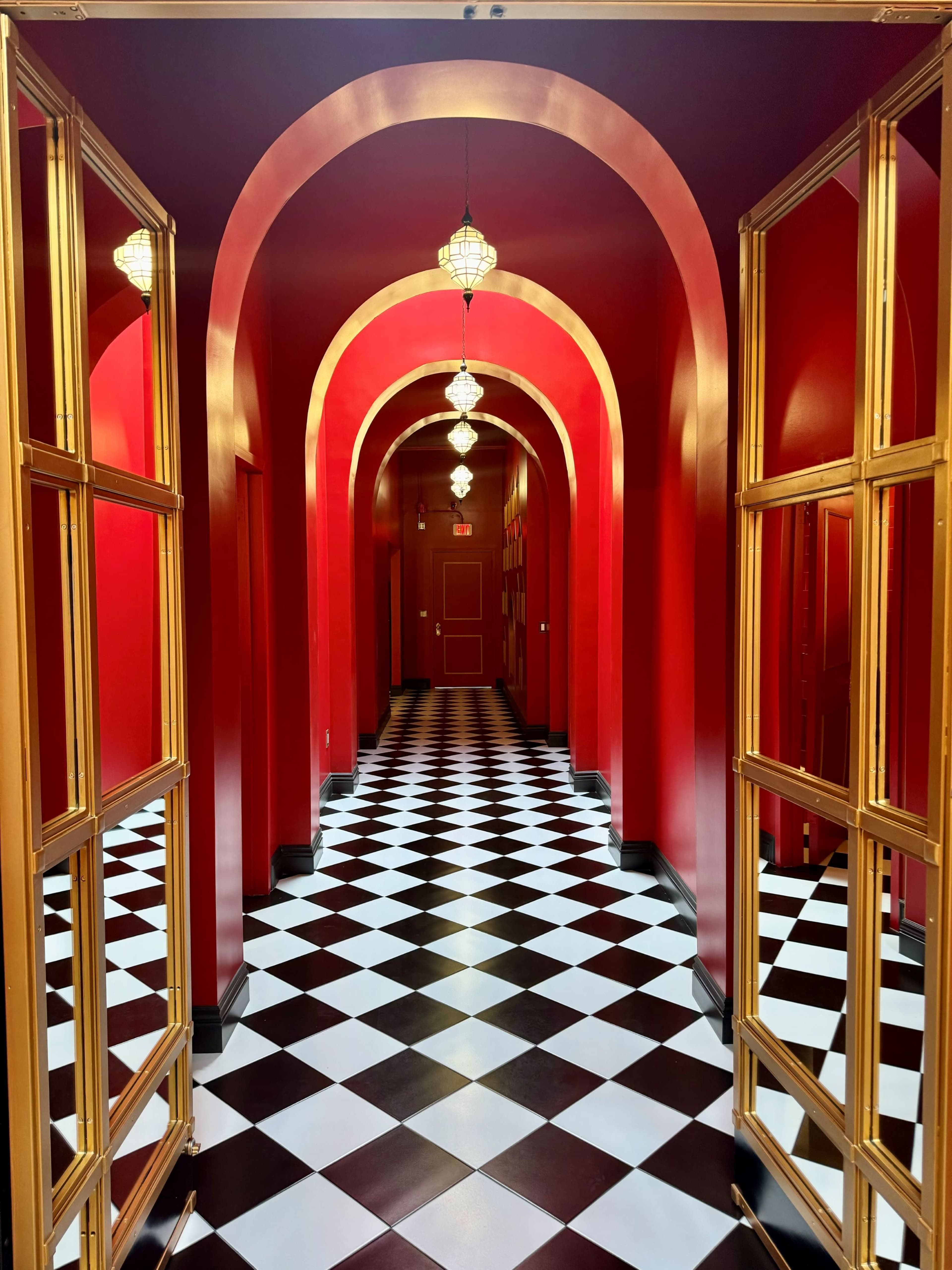 A hallway features a red and black checkered floor, arches with golden trim, and hanging light fixtures.