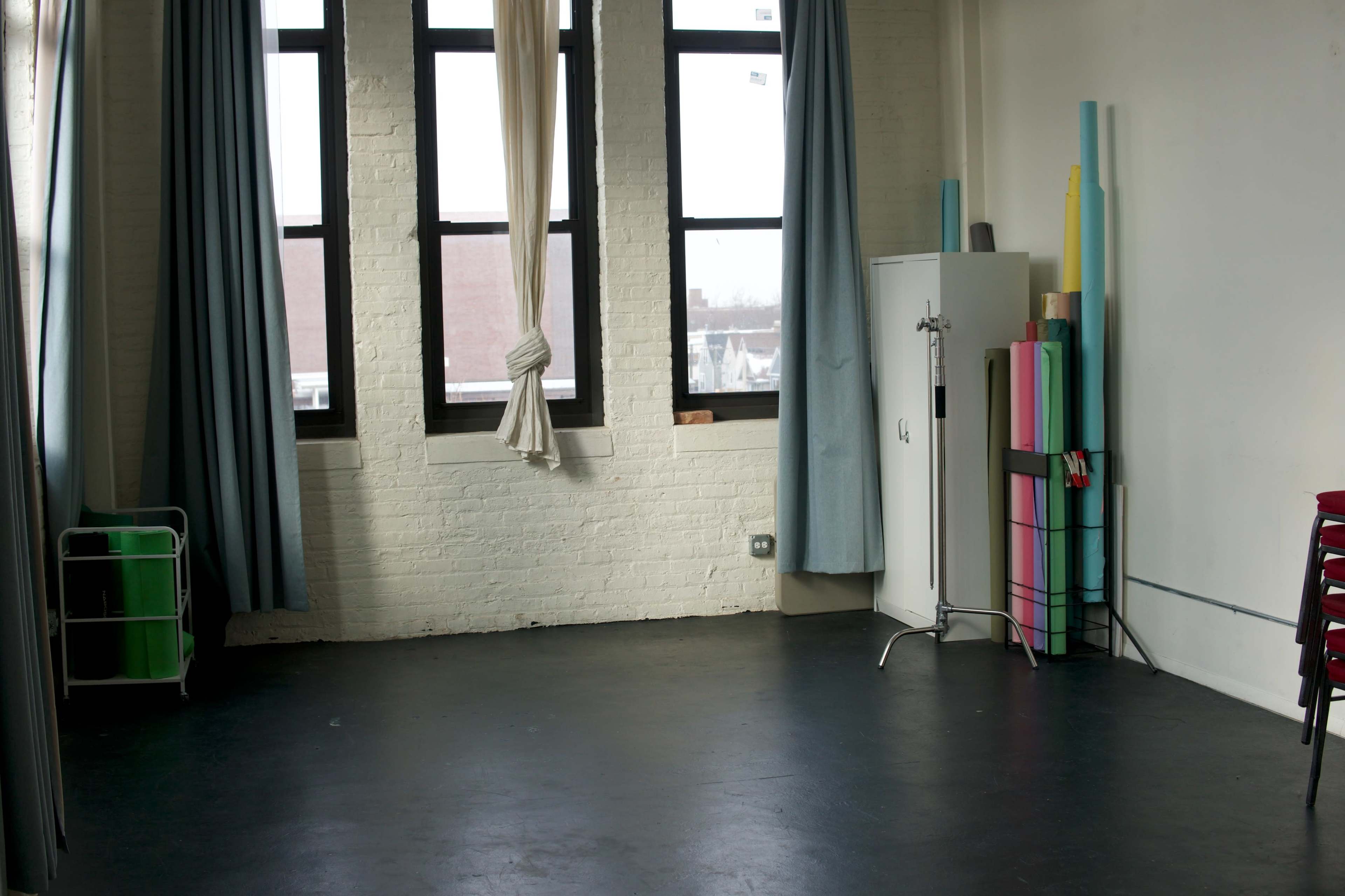 The image shows a spacious studio room with large windows, light-colored walls, and a mix of colorful props stored in the corner.