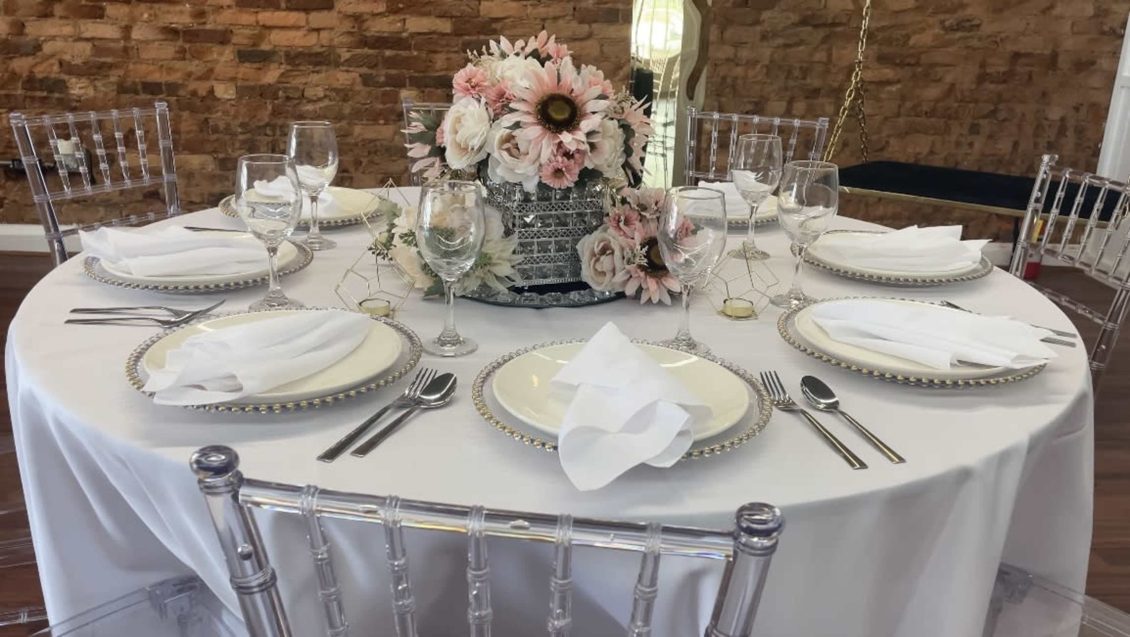 A round banquet table is elegantly set with white dinnerware, glassware, silverware, and a floral centerpiece.