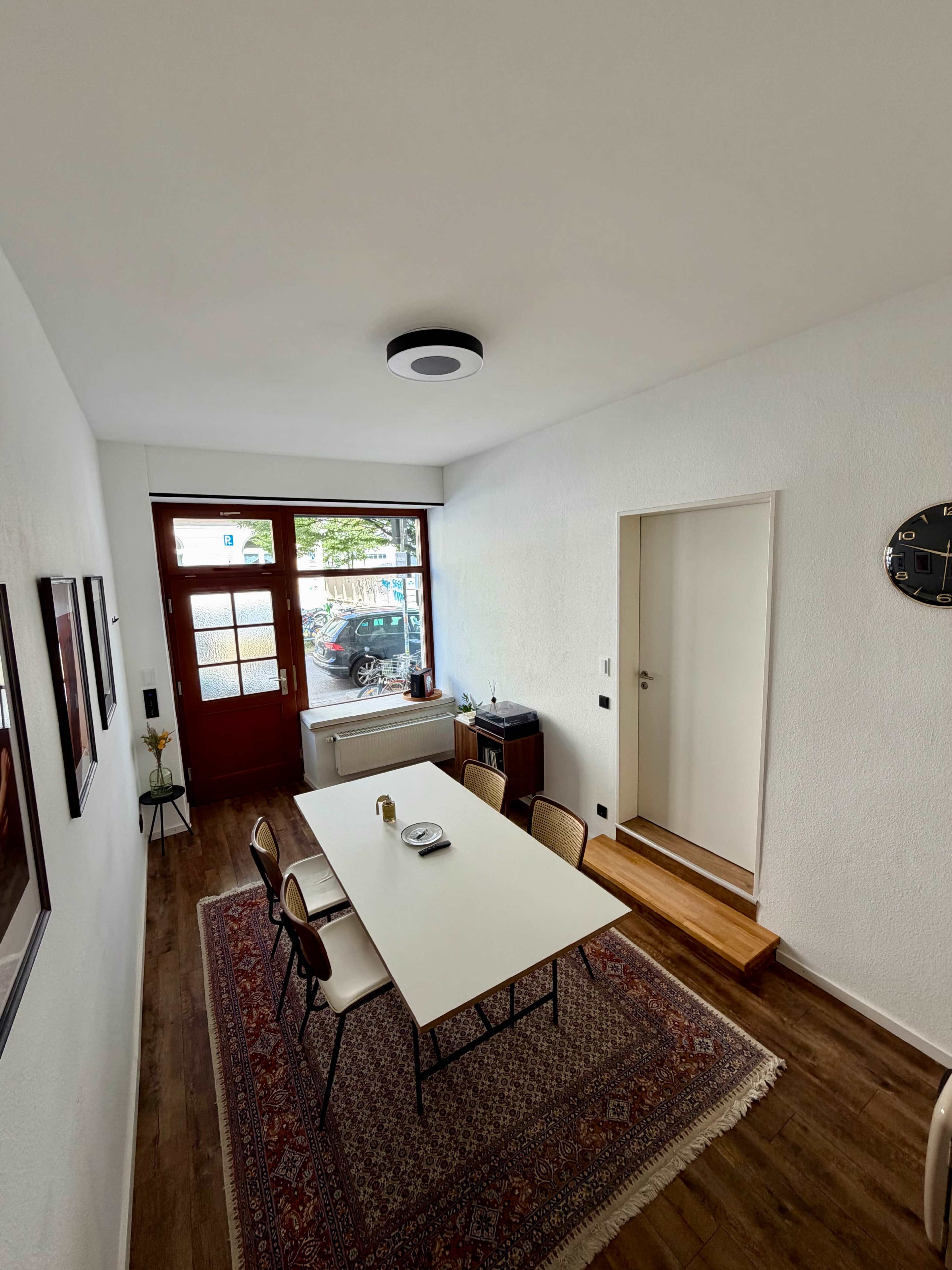 The image shows a modern dining area with a rectangular table, four chairs, and a doorway leading outside, featuring hardwood flooring and a large window.