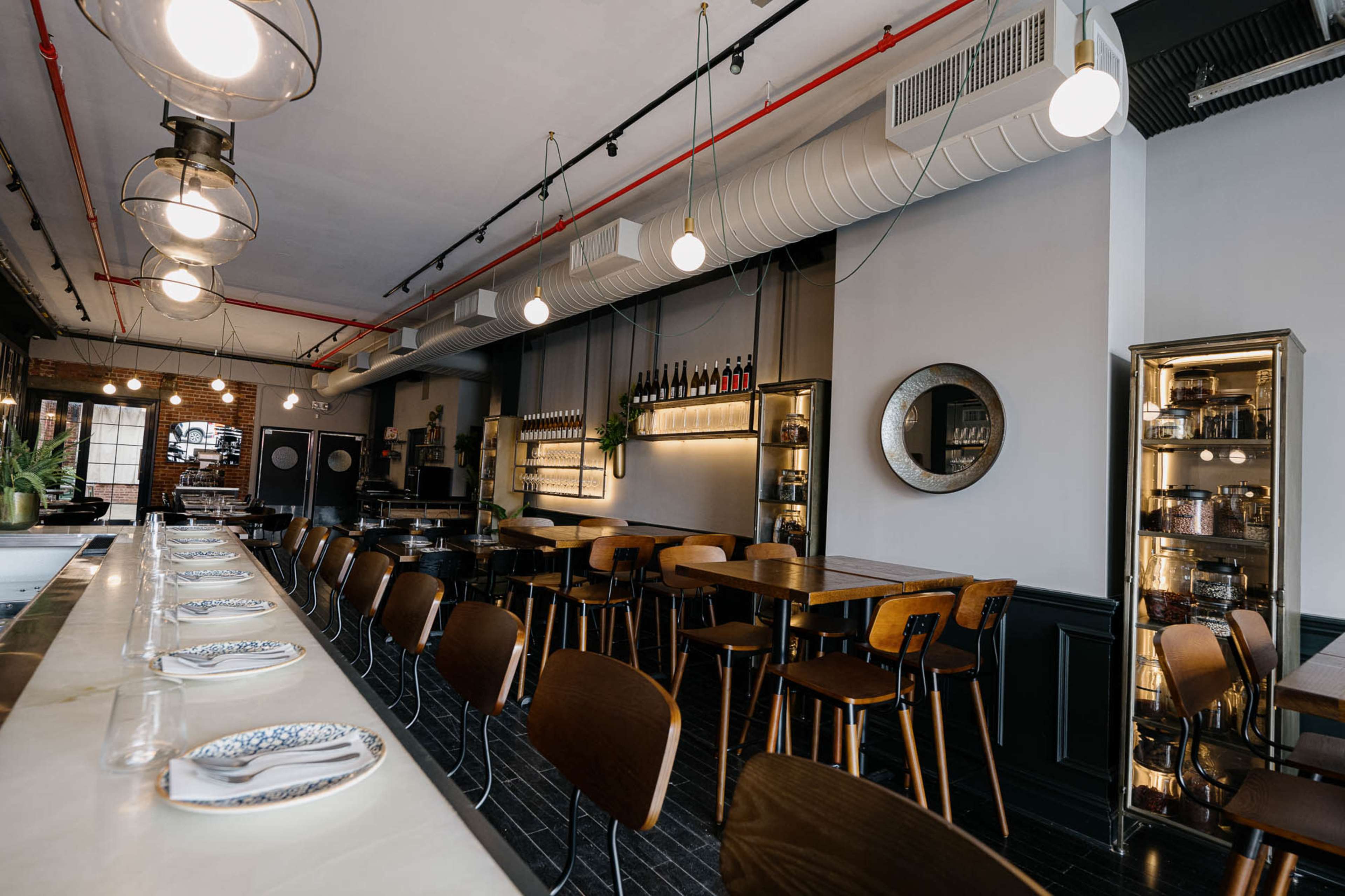 The image shows a modern restaurant interior with wooden tables, high-backed chairs, and ambient lighting fixtures.