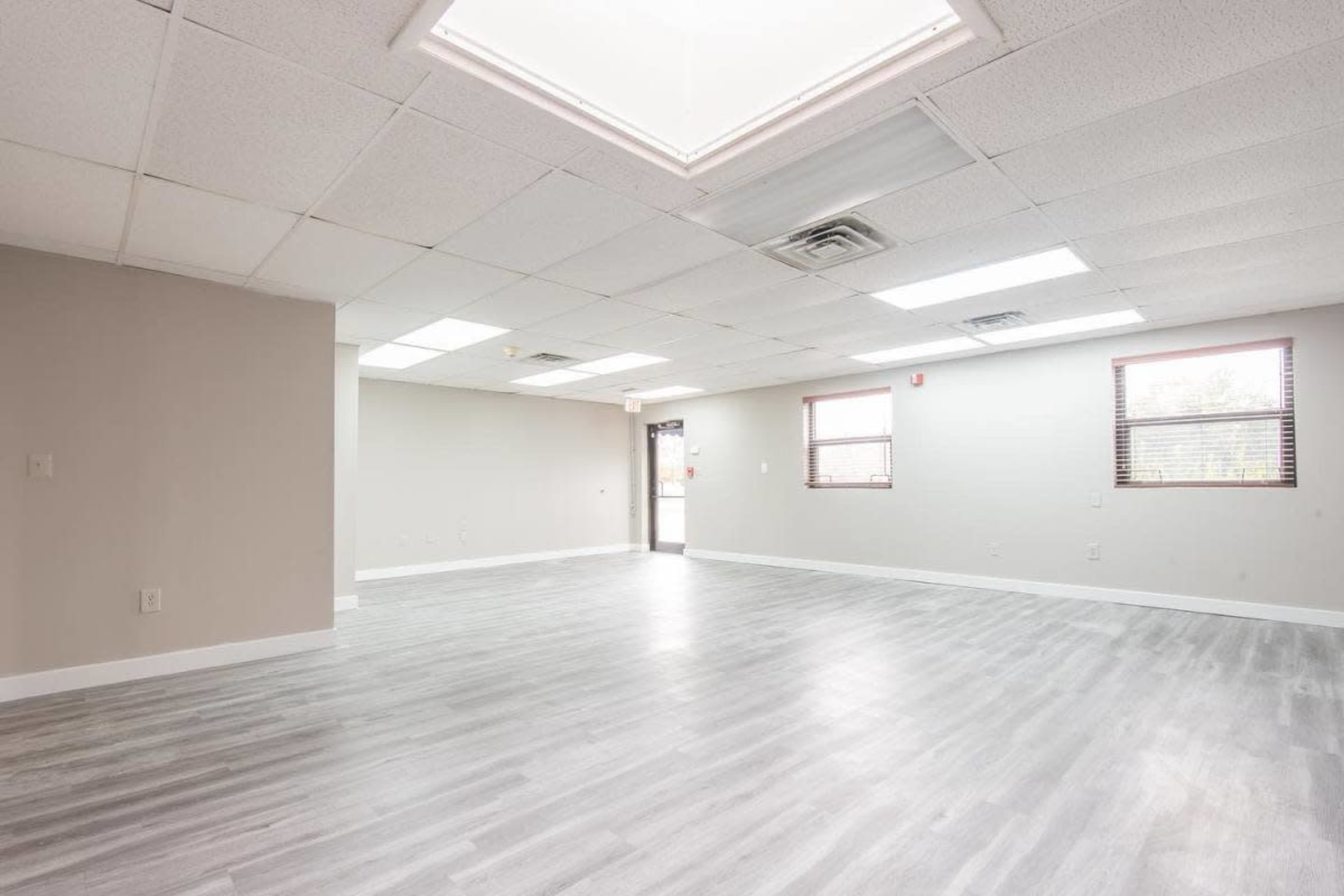 A spacious, empty room with gray laminate flooring and a ceiling skylight.