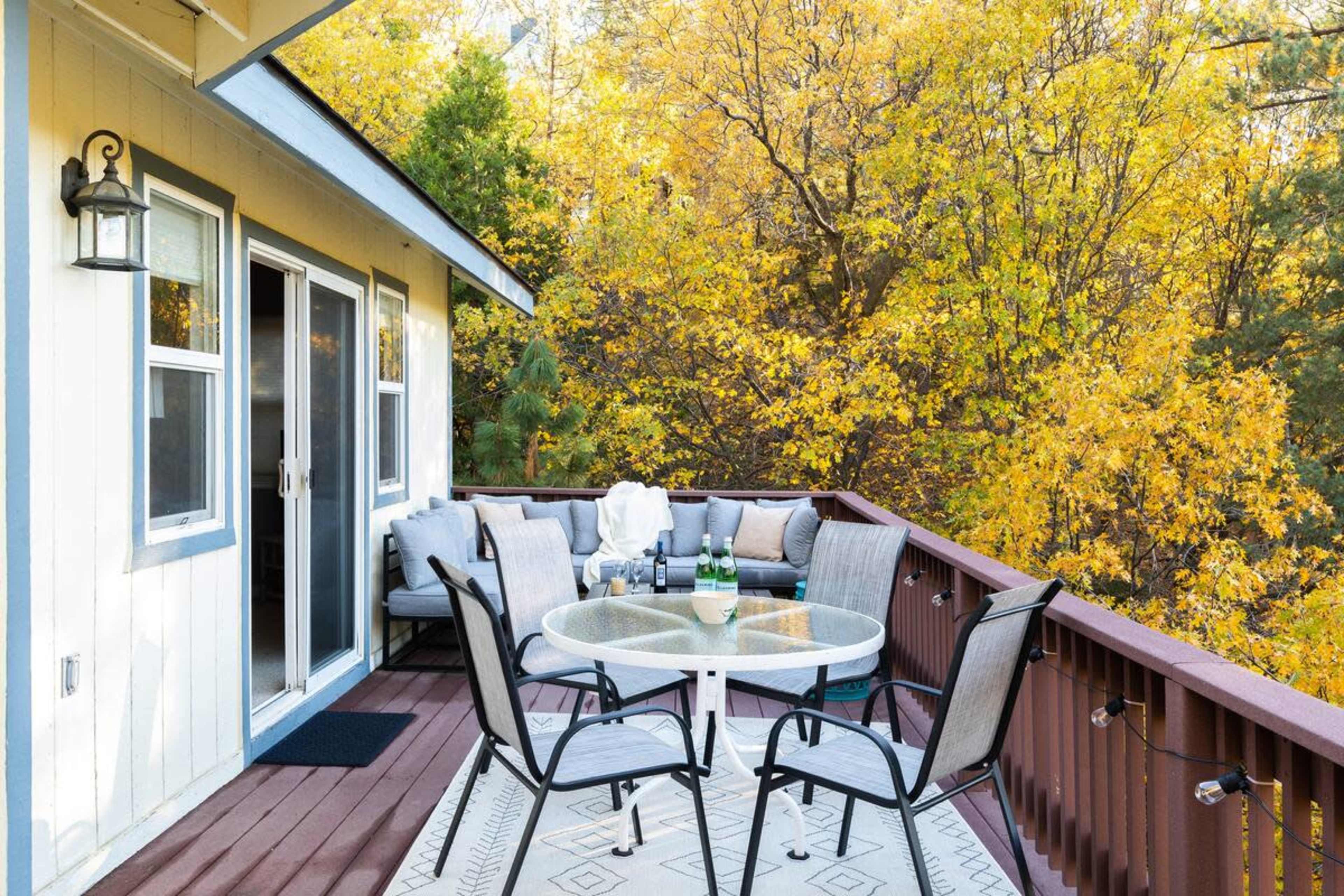 A cozy balcony features a round glass table with chairs, overlooking a backdrop of vibrant autumn foliage.
